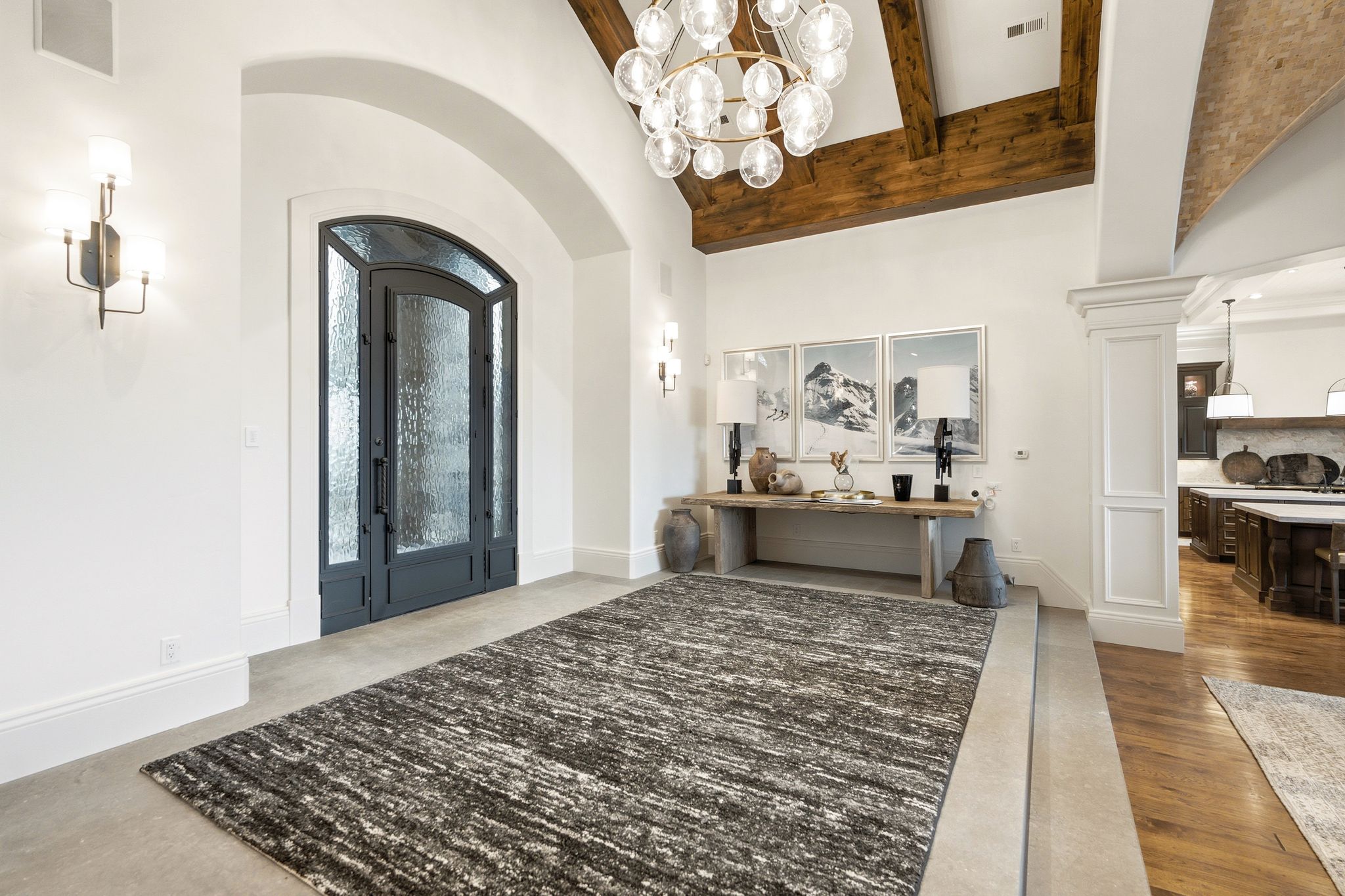 Grand entryway featuring a vaulted ceiling with exposed wood beams, a statement chandelier, and an arched entry door with frosted glass panels