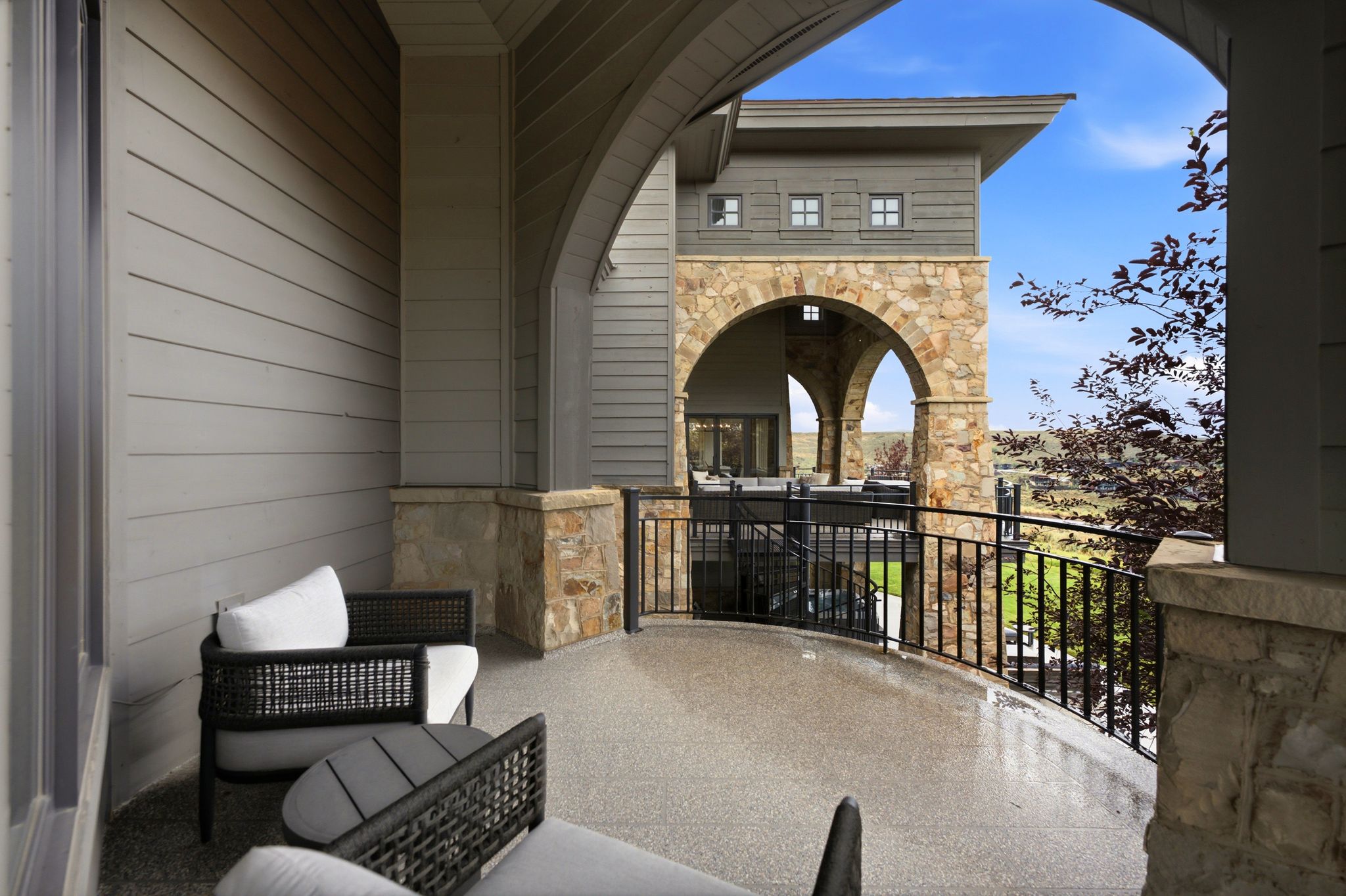 Curved balcony featuring a textured floor, black metal railing, and stone accents