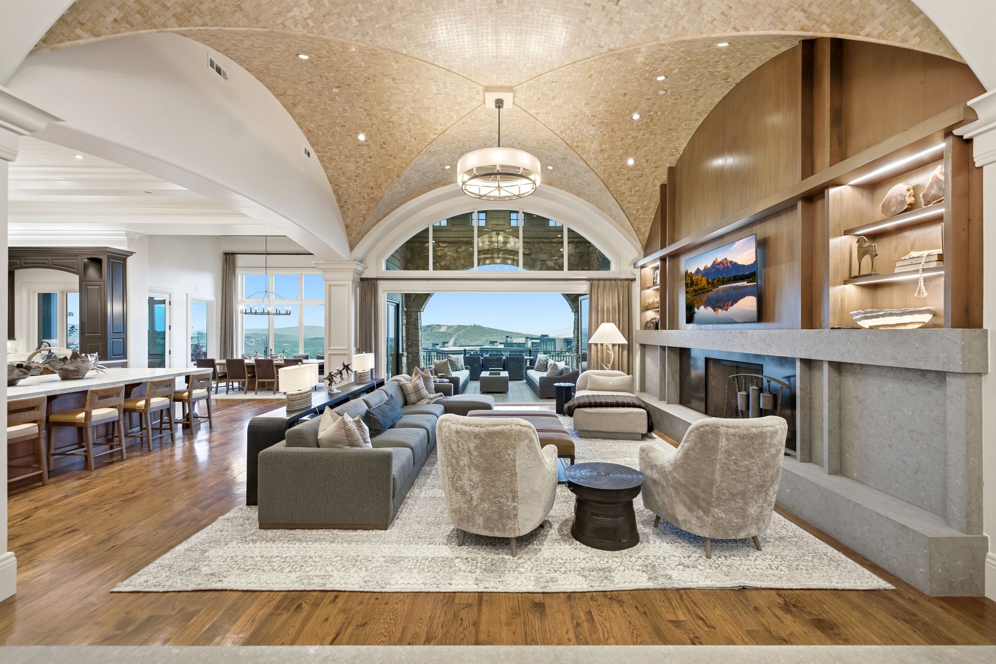 Vaulted ceiling with tile finish, hardwood flooring, built-in media center with shelving, fireplace, and arched glass doors opening to an exterior space