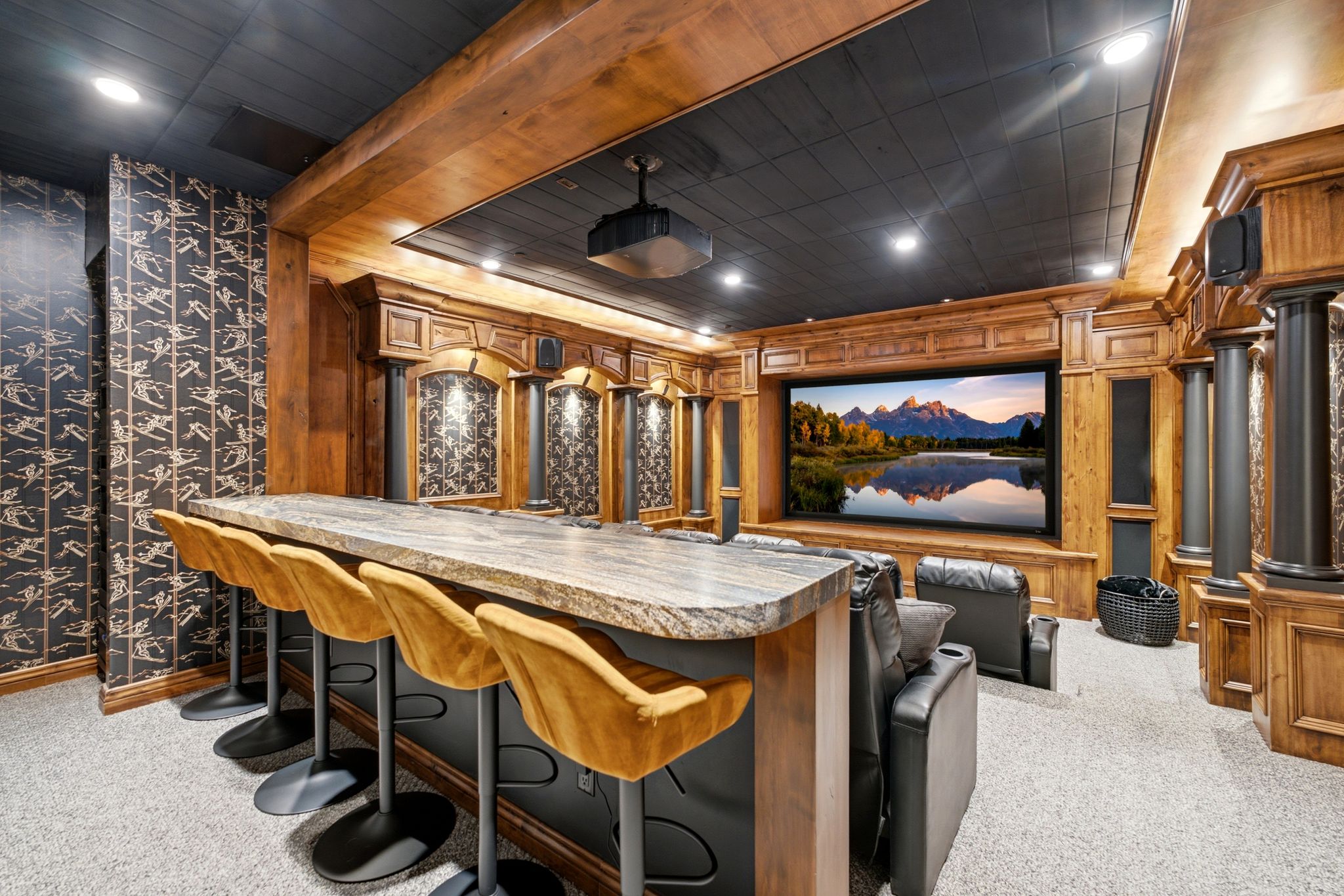 Dedicated home theater featuring a large projection screen, wood-paneled walls, built-in bar with stone countertop, dark paneled ceiling, and recessed lighting