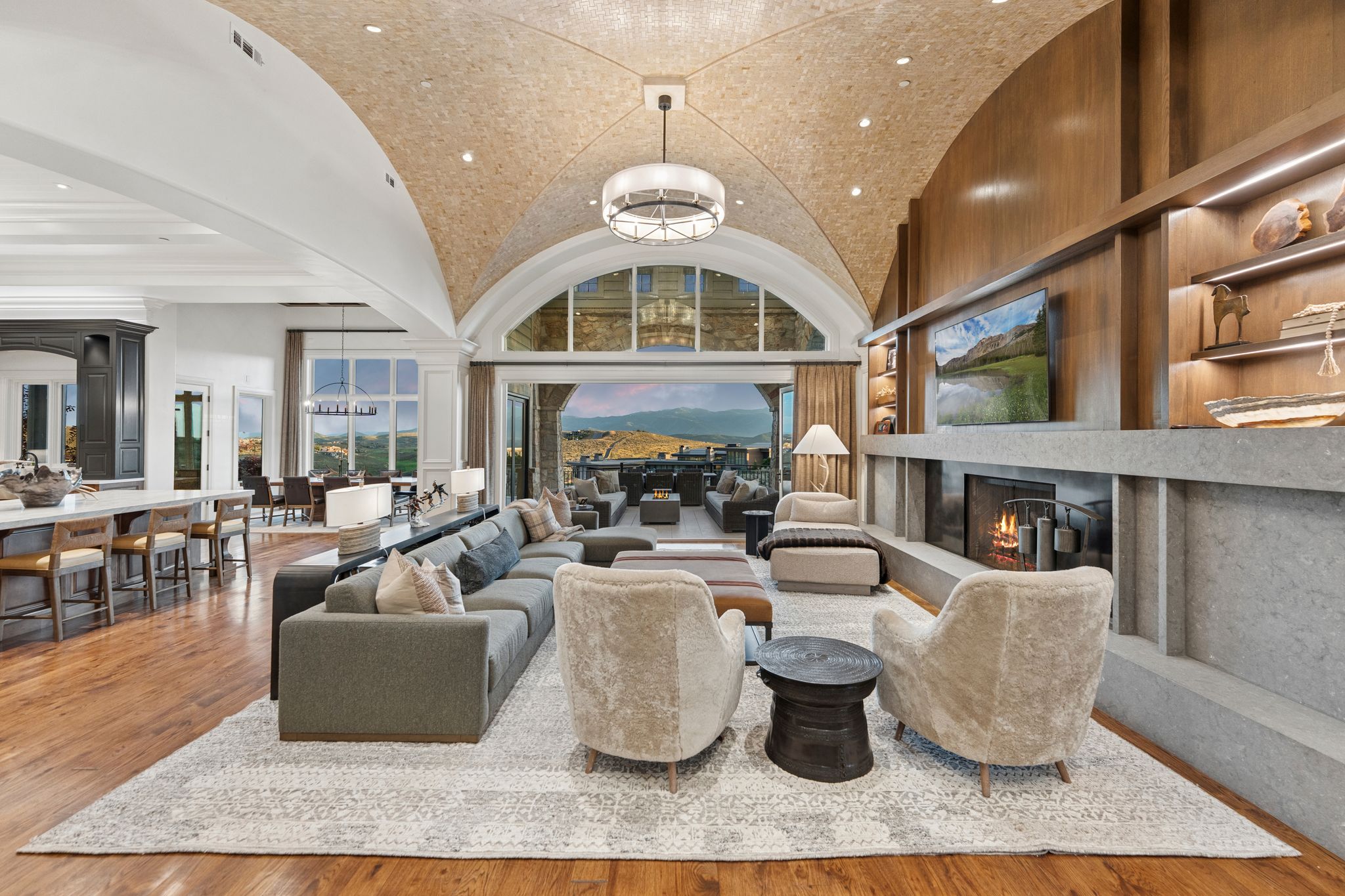Spacious living area featuring a vaulted wood-finish ceiling, a stone fireplace, wood-finish flooring, a built-in entertainment center with shelving, and large arched windows
