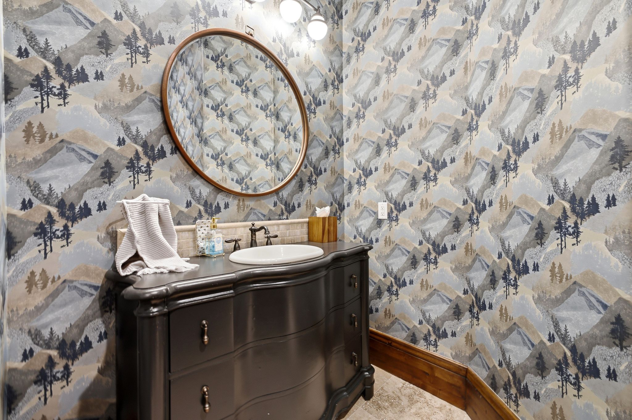 Powder room featuring a dark vanity with an integrated white basin, a bronze-finish faucet, and a round wood-frame mirror