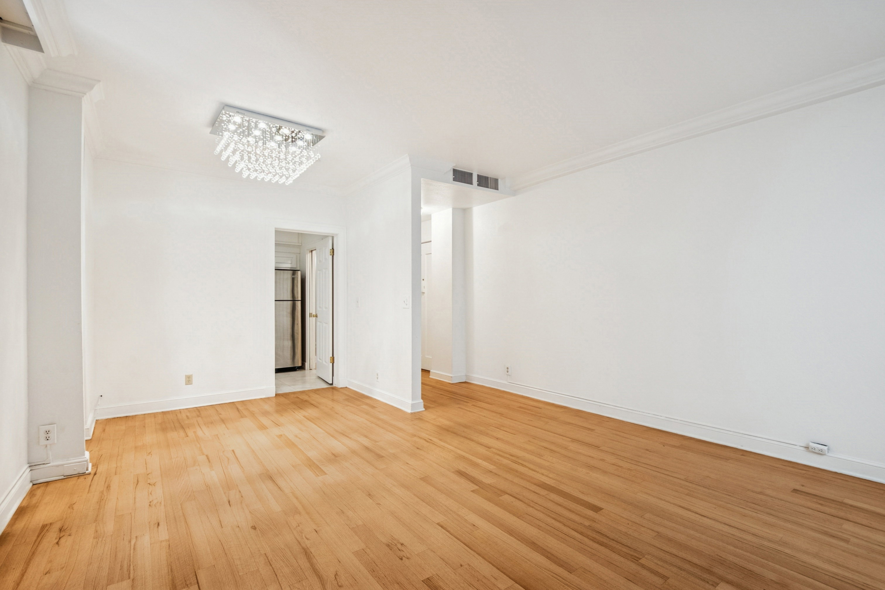 Open-concept living space featuring wood-finish flooring, white painted walls, a decorative ceiling light fixture, and crown molding