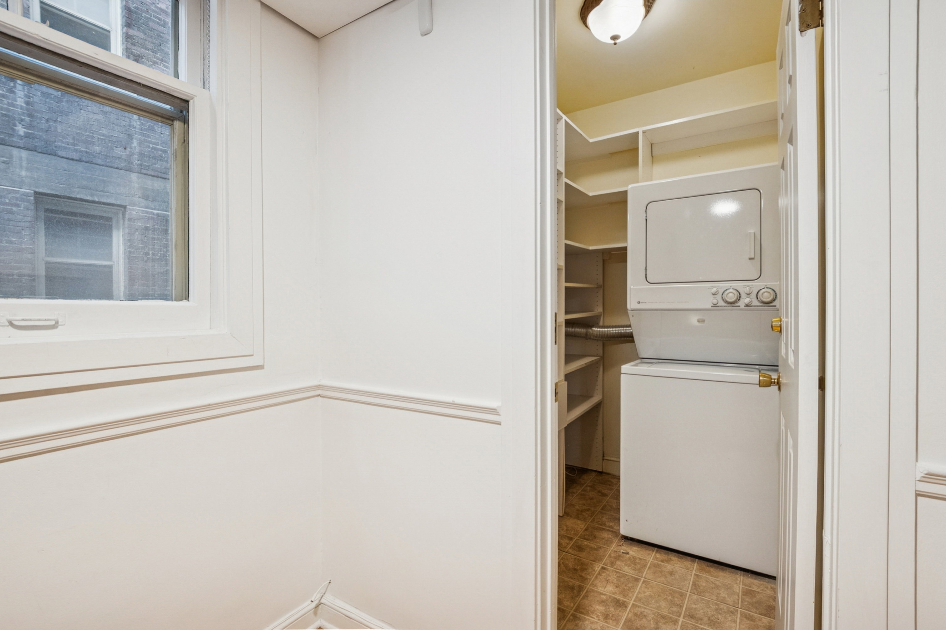 Dedicated laundry area with a stacked washer and dryer, complemented by built-in shelving and tile flooring