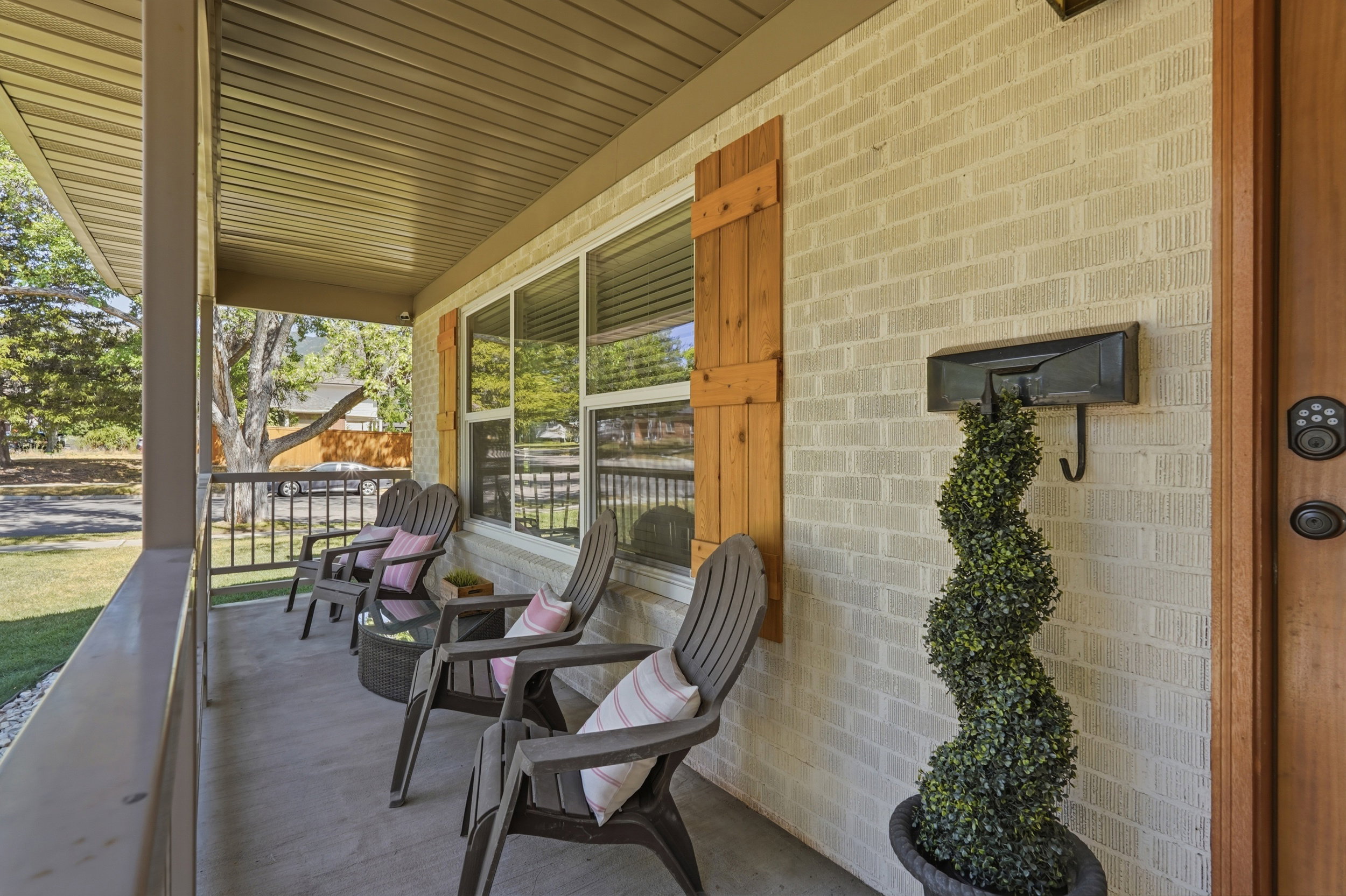 Covered front porch featuring a light-colored brick exterior, wood-finish window shutters, a dark wood-finish entry door, and multi-pane windows