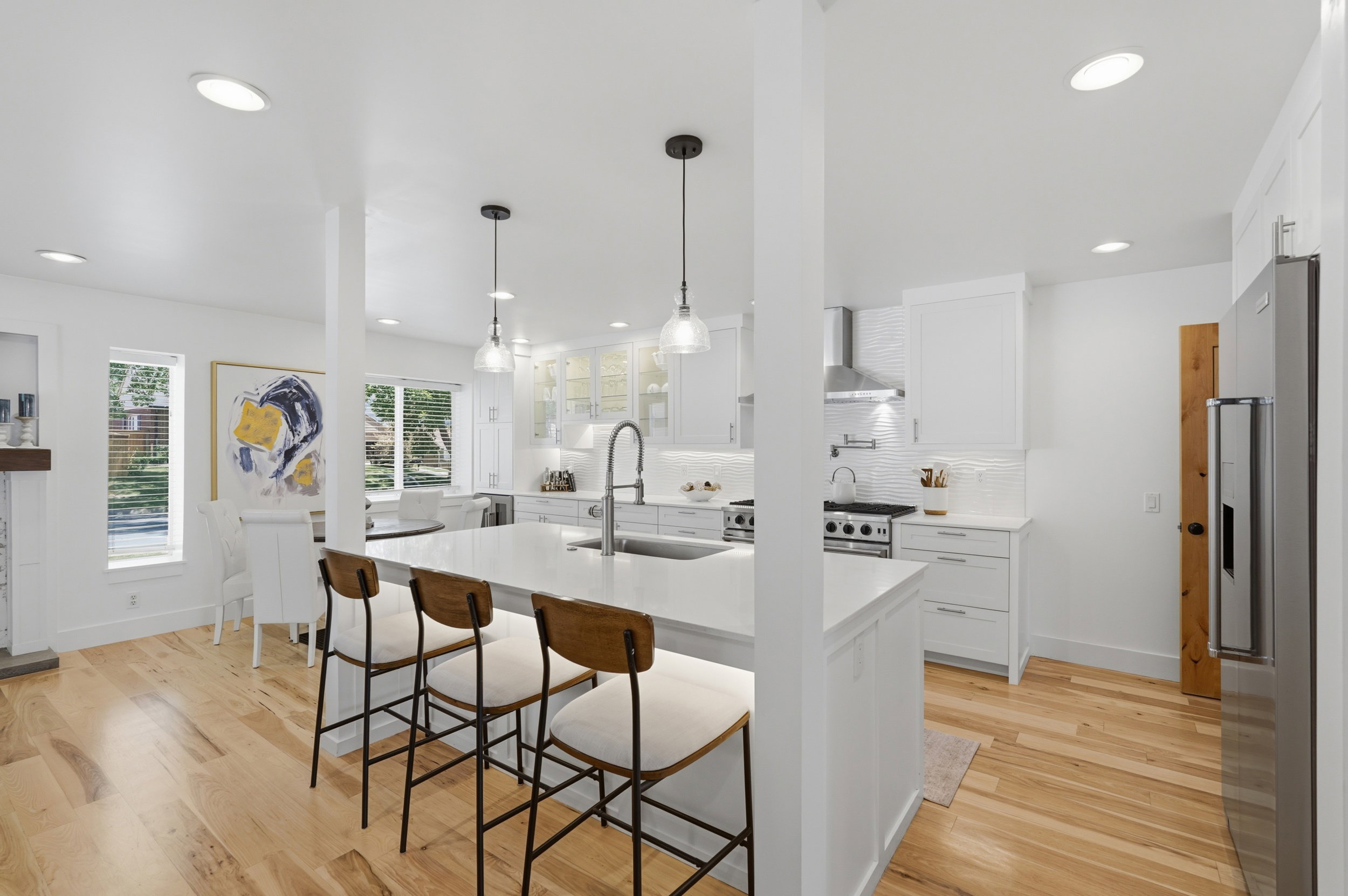 Contemporary kitchen featuring a large central island with seating, stainless steel appliances, white cabinetry, and wood-finish flooring