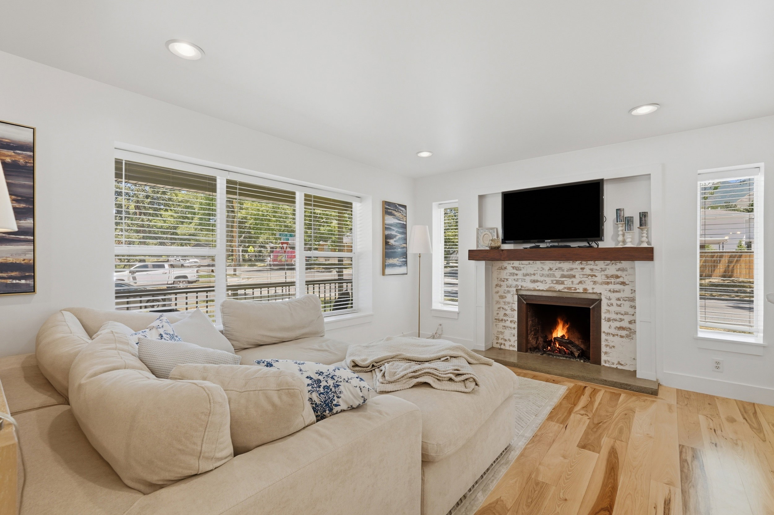 Living area featuring a brick-surround fireplace with a wood mantel, recessed lighting, wood-finish flooring, and multiple windows