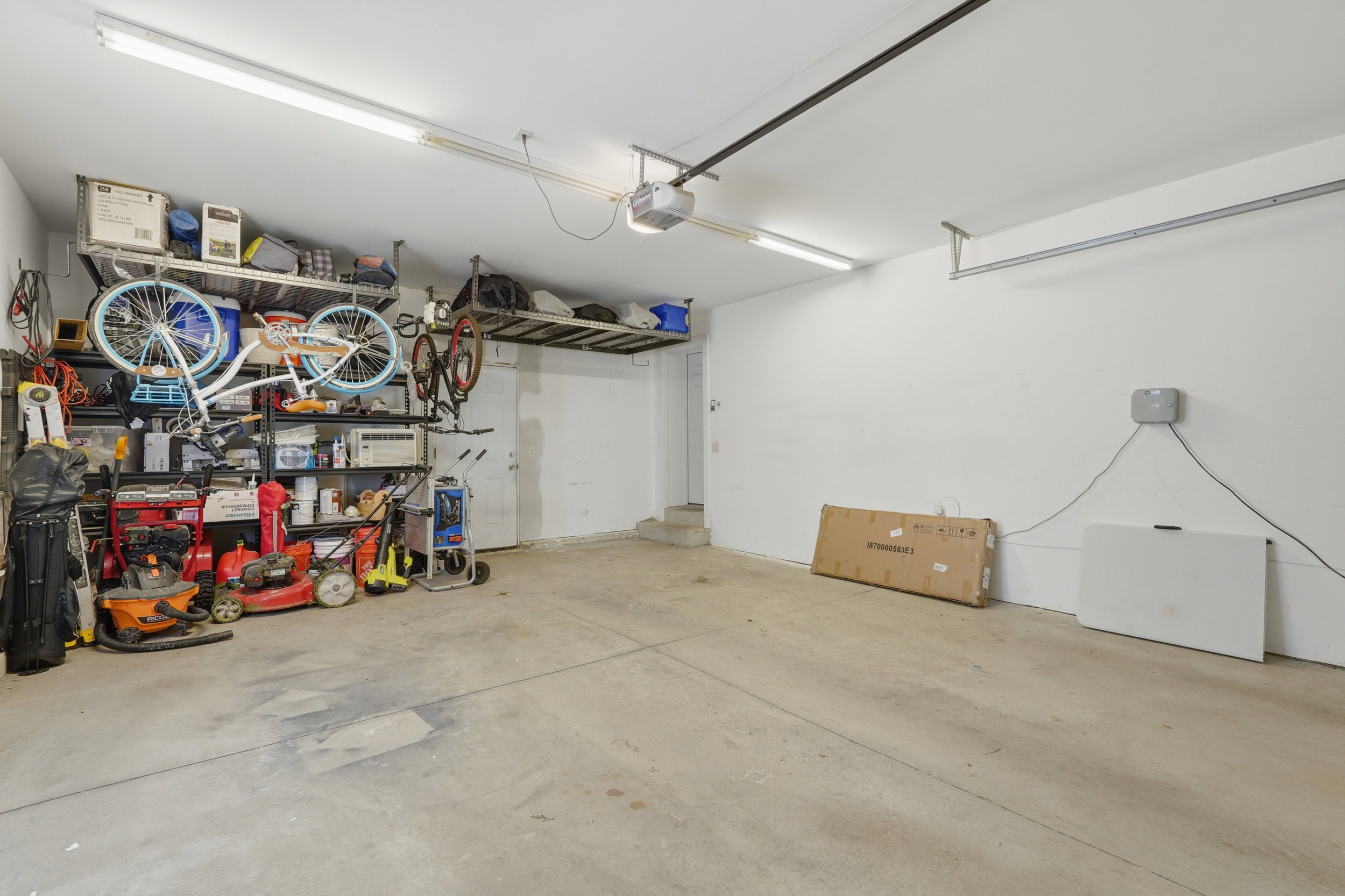 Spacious garage with a concrete floor, white walls, and overhead fluorescent lighting