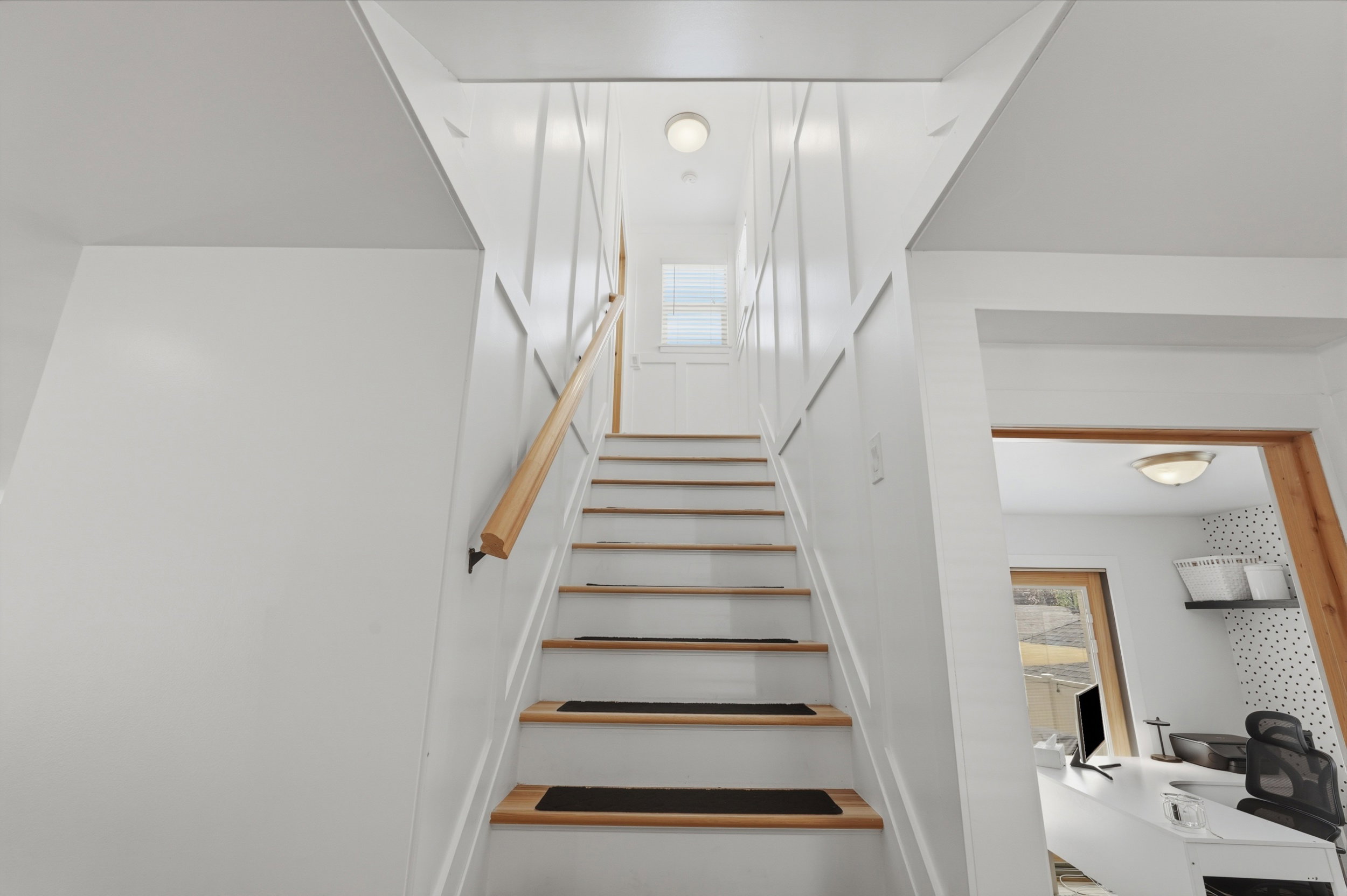 Staircase featuring wood treads with dark risers, a natural wood handrail, and white paneled walls. Goes up to the owners suite on  Level 2.