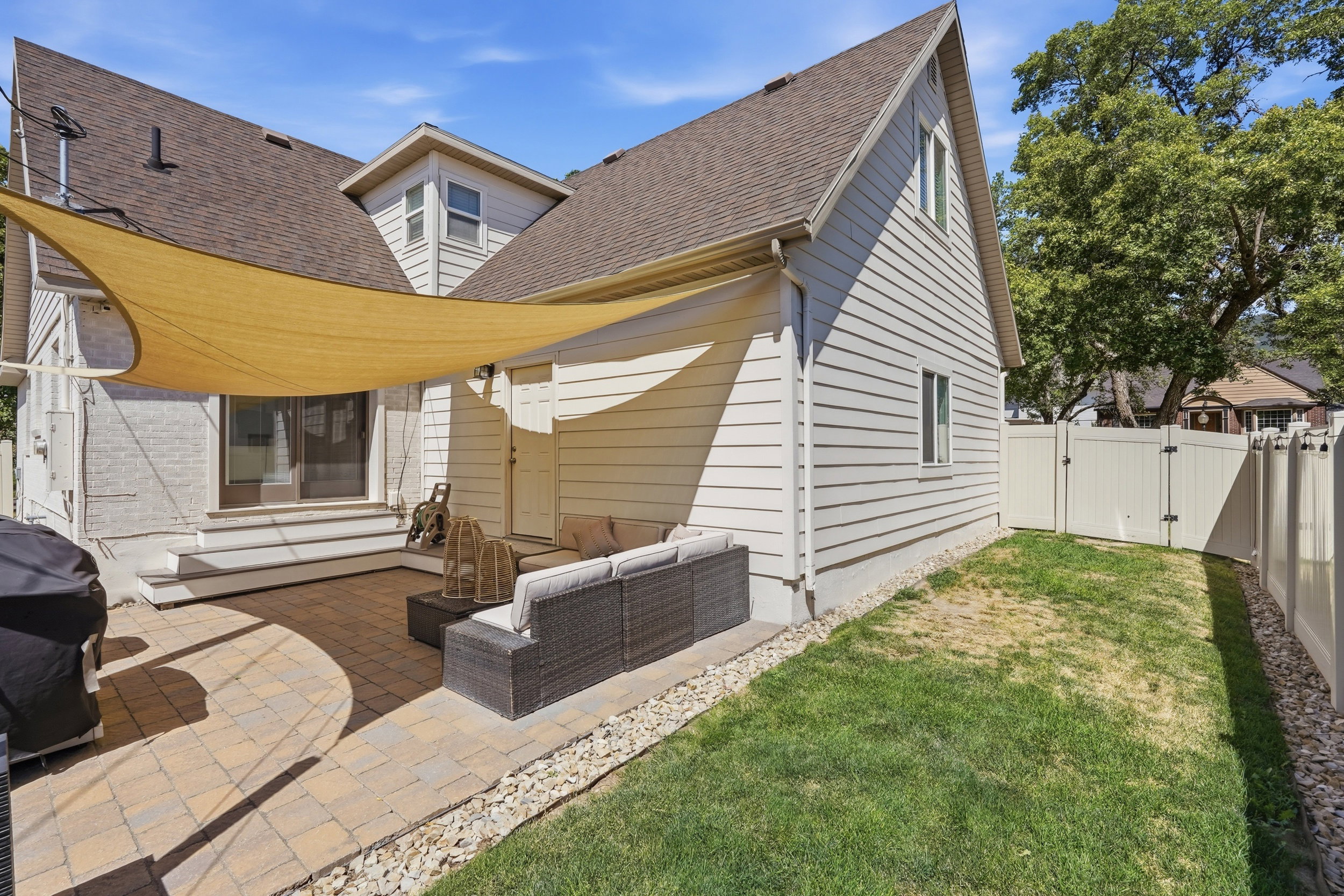 Expansive paver patio featuring a sun shade structure, direct access to the interior via double glass doors, and a vinyl privacy fence enclosing the yard