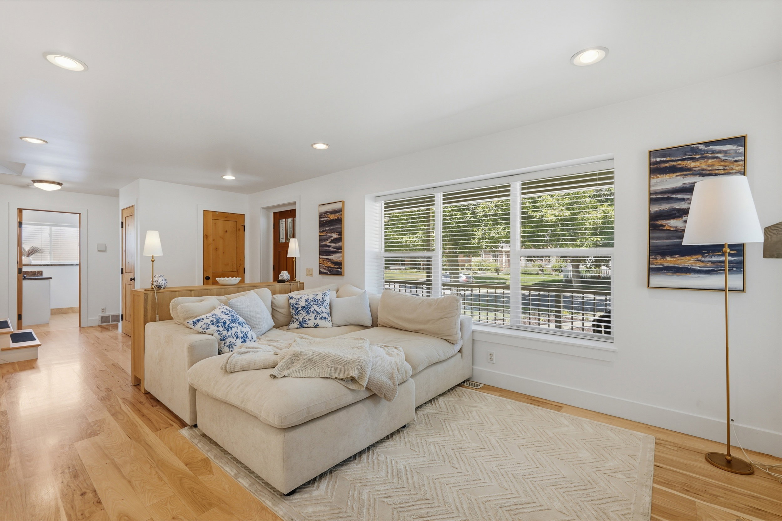 Light wood-finish flooring extends through this bright room, featuring recessed lighting and a large window with white blinds