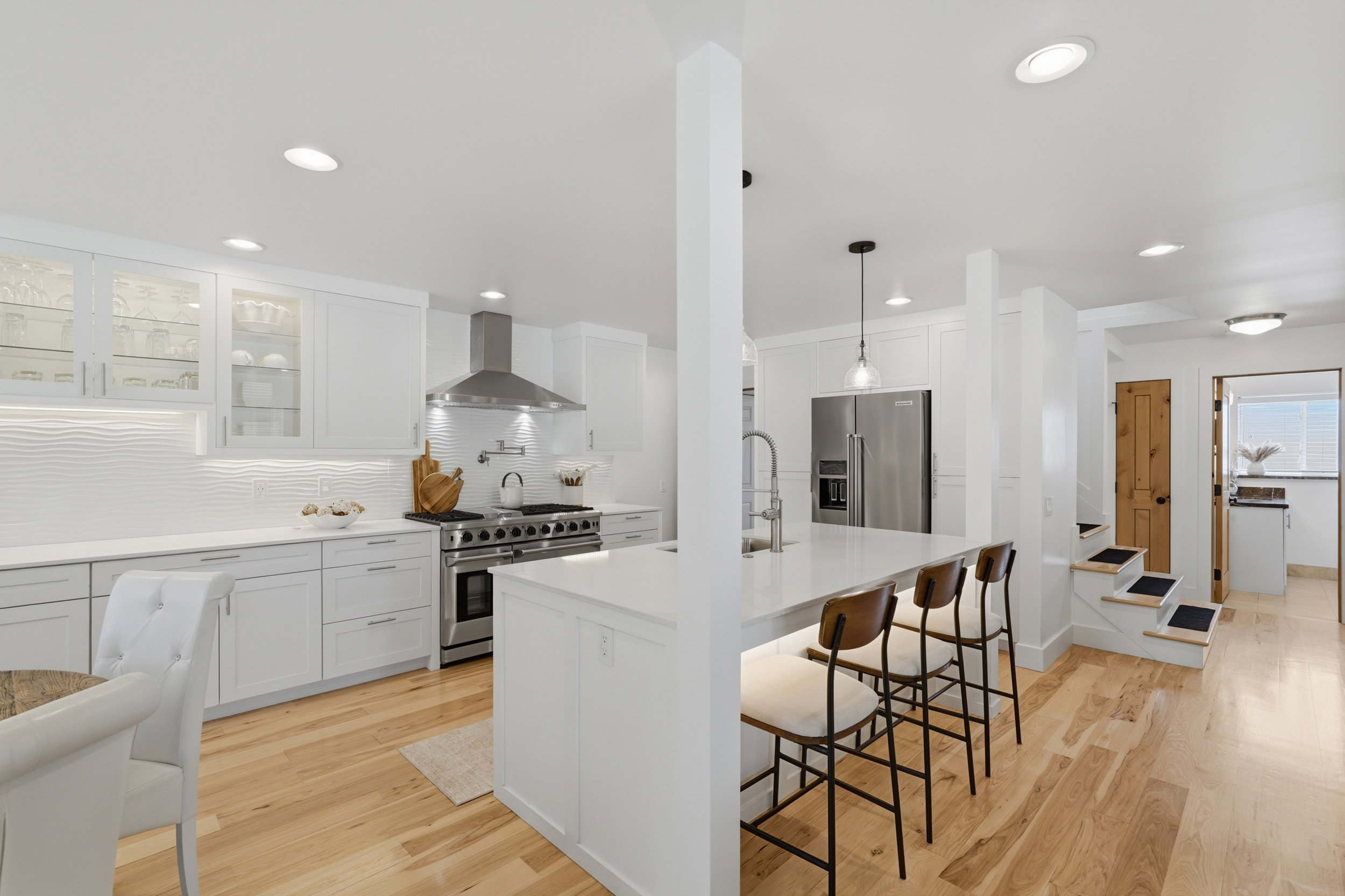 Bright kitchen featuring white cabinetry, stainless steel appliances, a center island with bar seating, wood-finish flooring, and recessed lighting