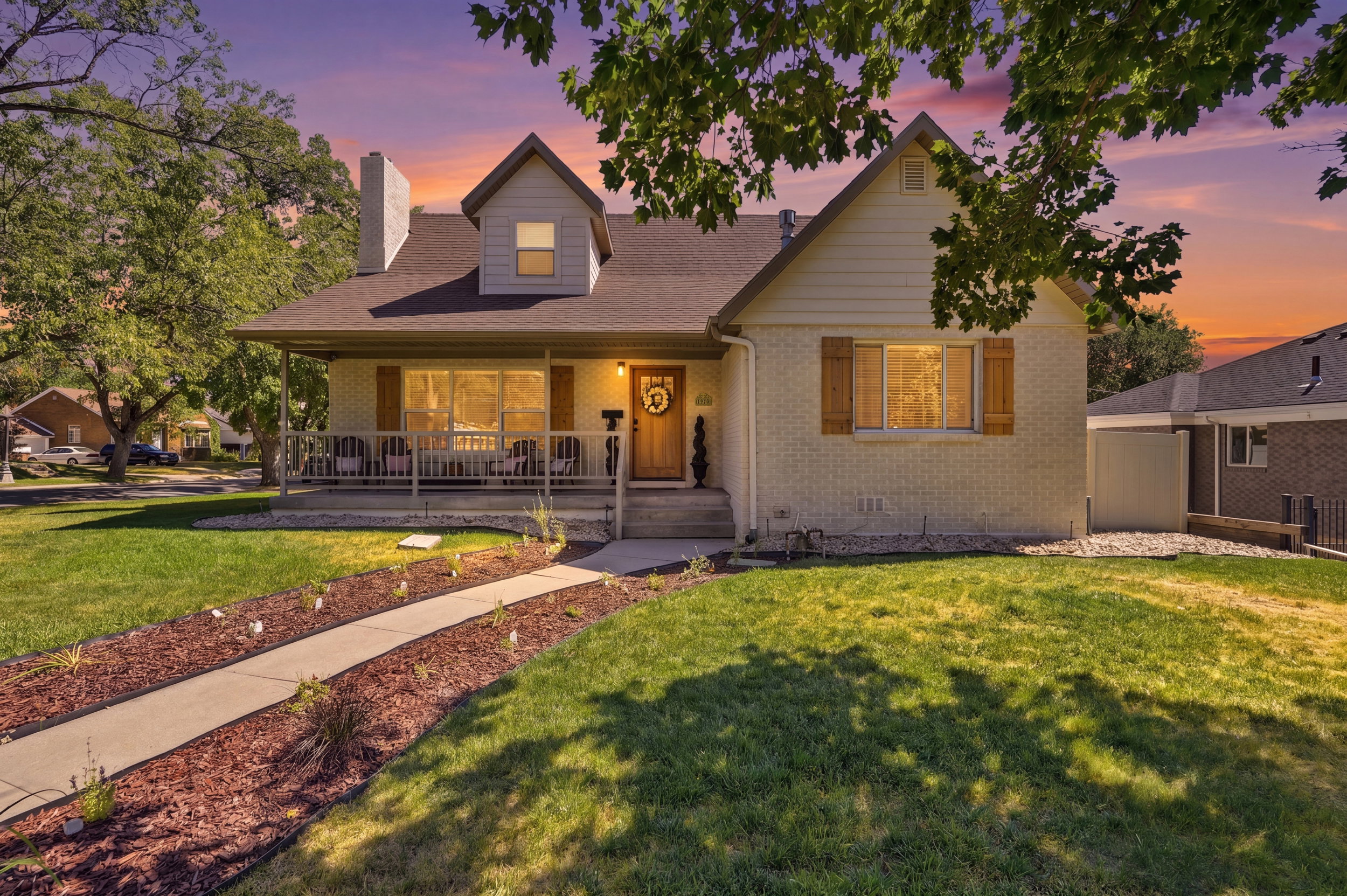 Traditional-style home featuring a covered front porch with railings, light-colored brick exterior, and a dormer window