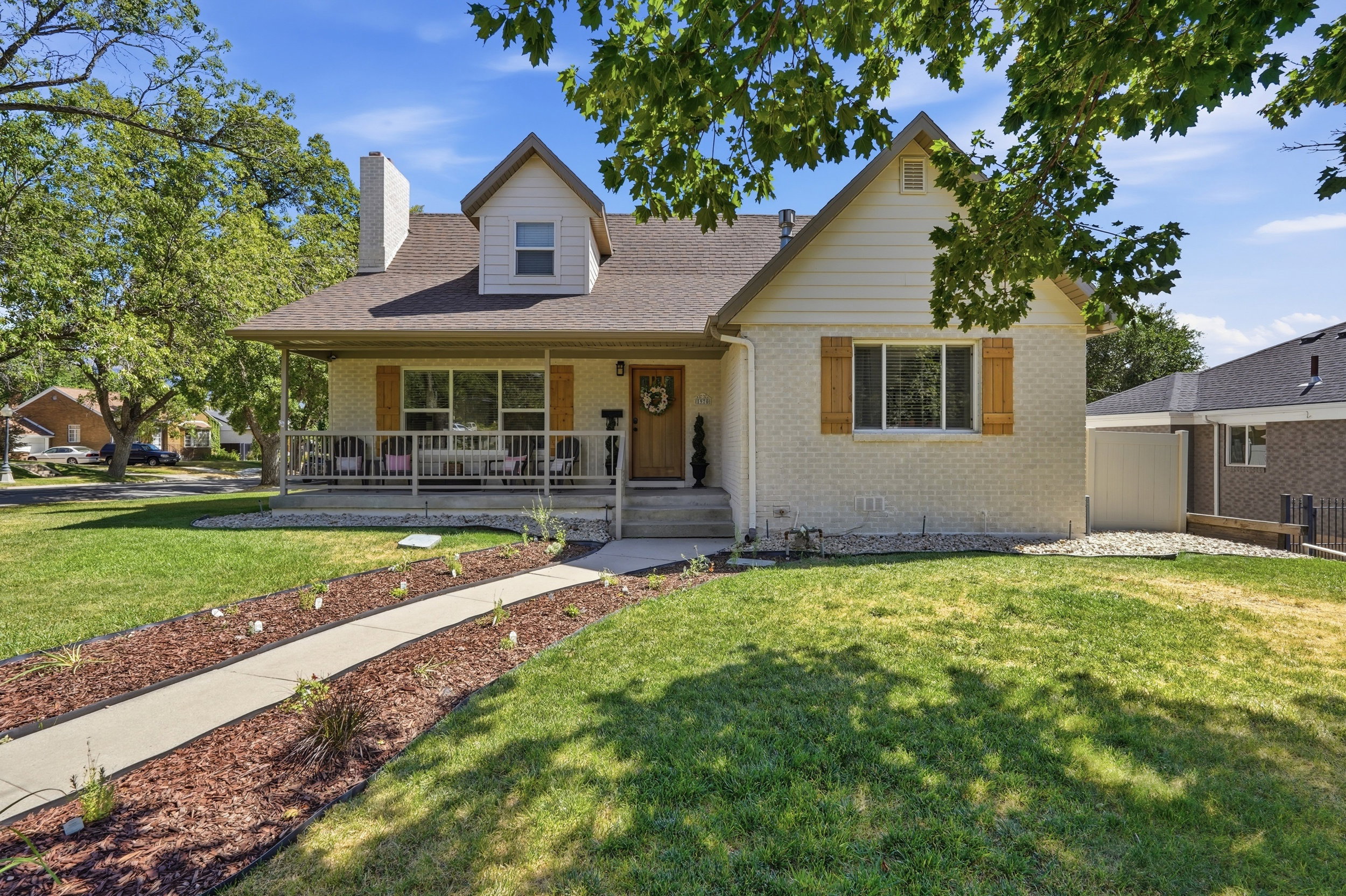 Charming exterior with light brick facade, gabled roofline, front porch, decorative shutters, and mature trees
