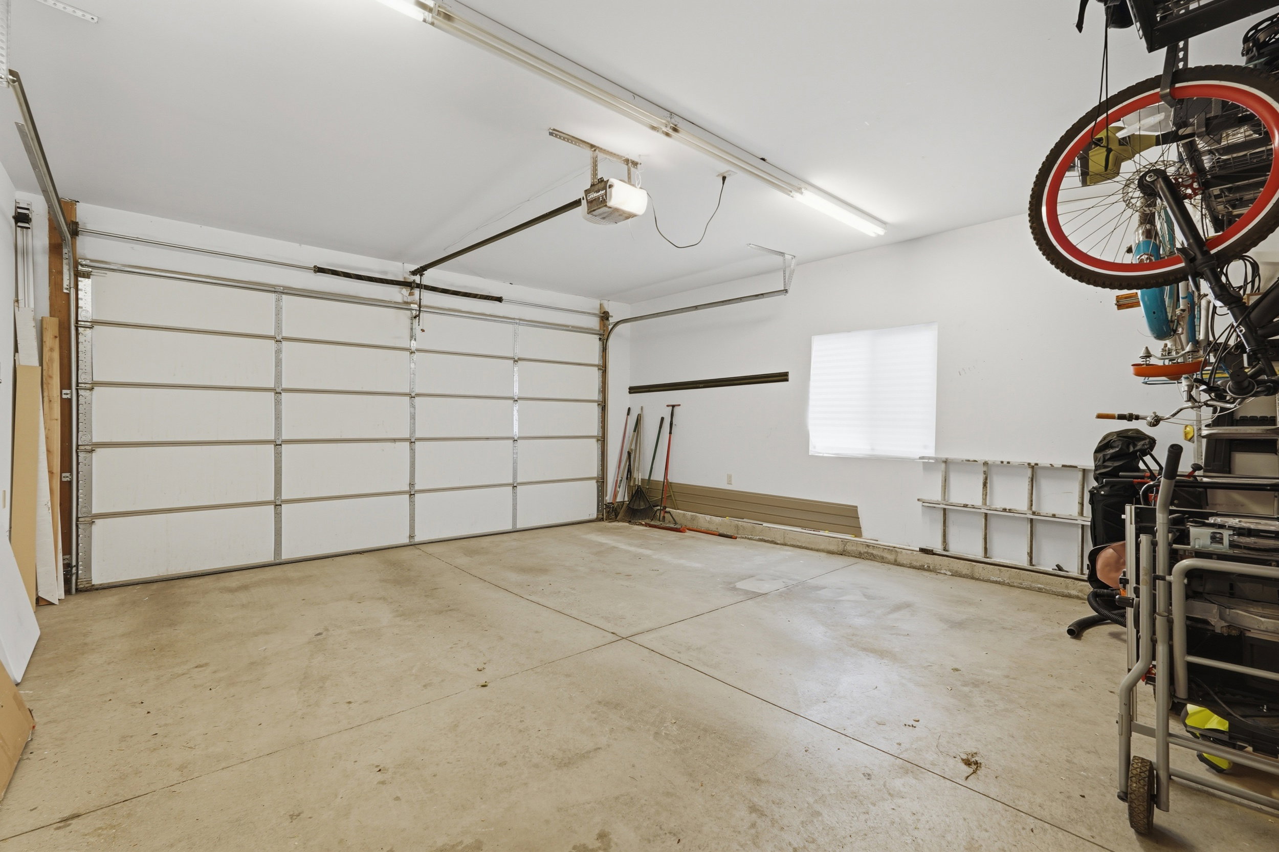Spacious garage featuring a concrete floor, overhead fluorescent lighting, and a window with blinds