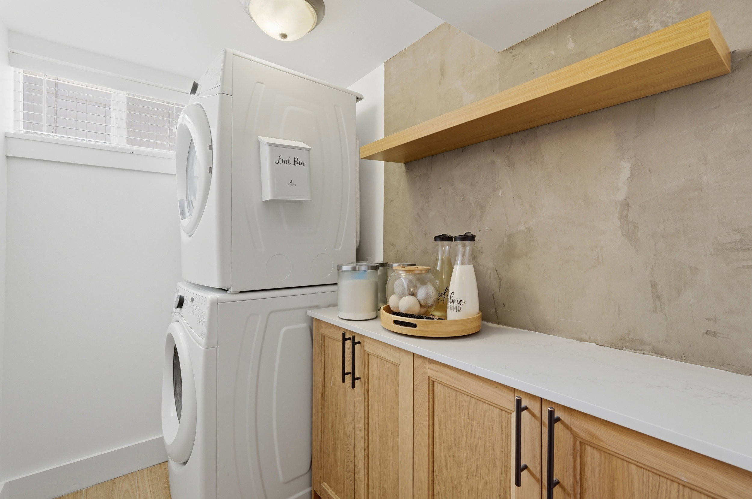 Dedicated laundry area featuring stacked appliances, a built-in wood-finish floating shelf, and white countertops