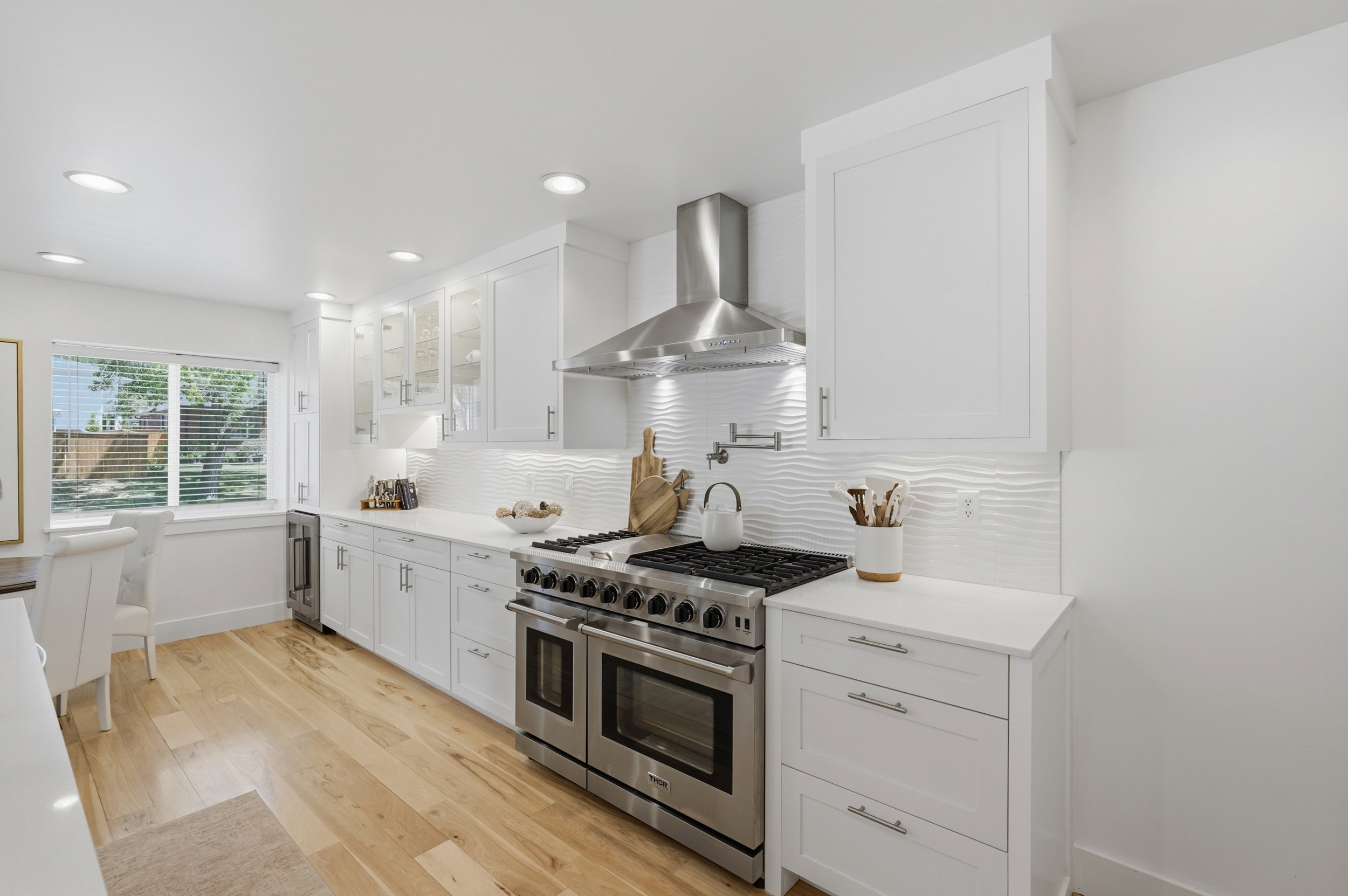 Bright kitchen featuring white shaker cabinetry, stainless steel professional-grade range, wood-finish flooring, white countertops, and a textured white tile backsplash