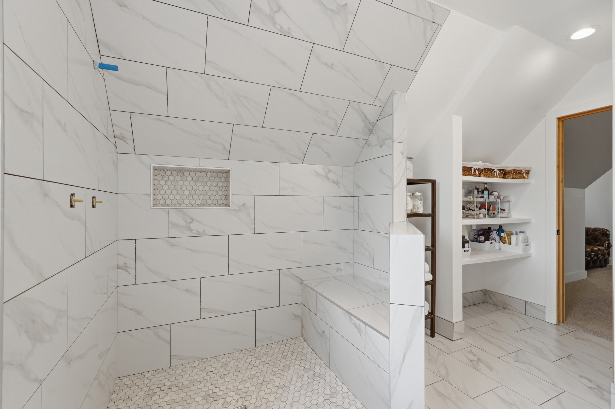 Spacious shower featuring large-format tile walls, hexagonal mosaic tile flooring, a built-in bench, and a recessed niche. Ensuite will be complete by Open House.
