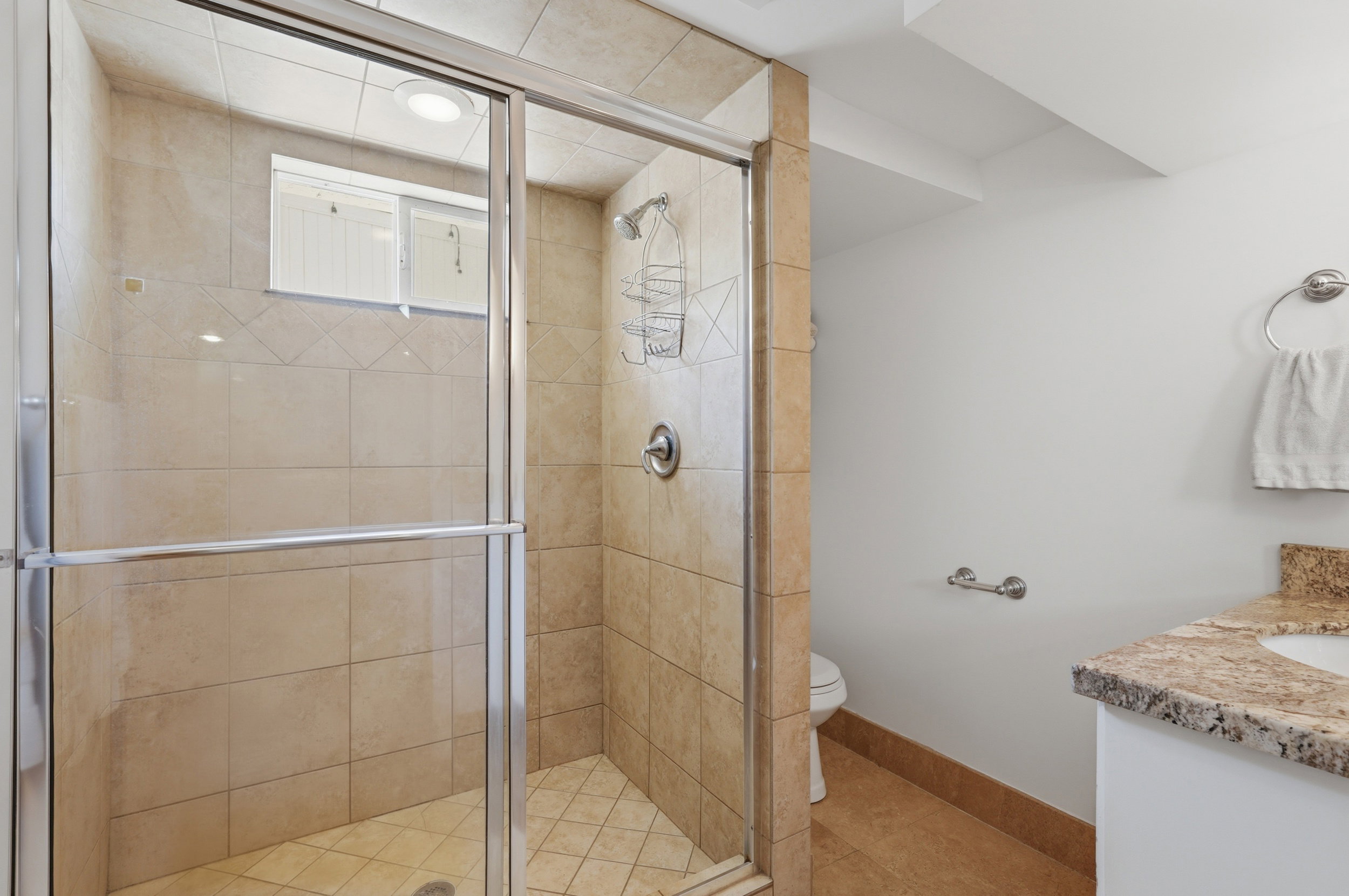 Glass-enclosed shower featuring light-toned tile walls and floor, complete with a shower head and grab bar