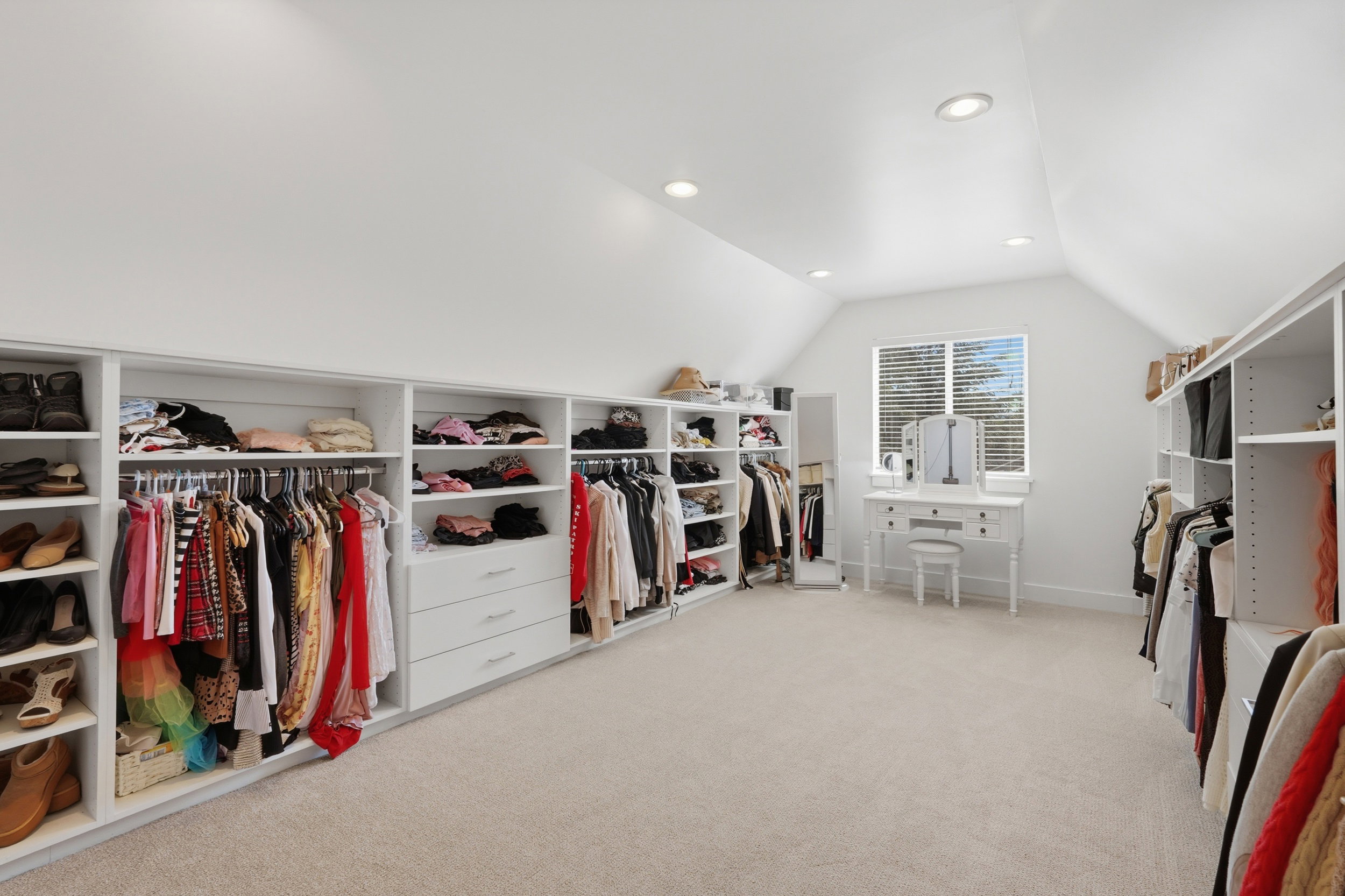 Spacious walk in closet with built-in white cabinetry, integrated hanging rods, and shelving