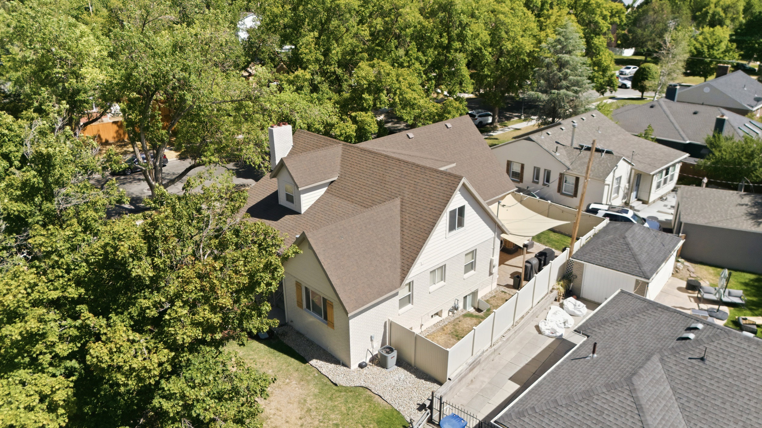 Residential property featuring a light-colored exterior, brown shingled roof, a prominent chimney, and multiple dormer windows