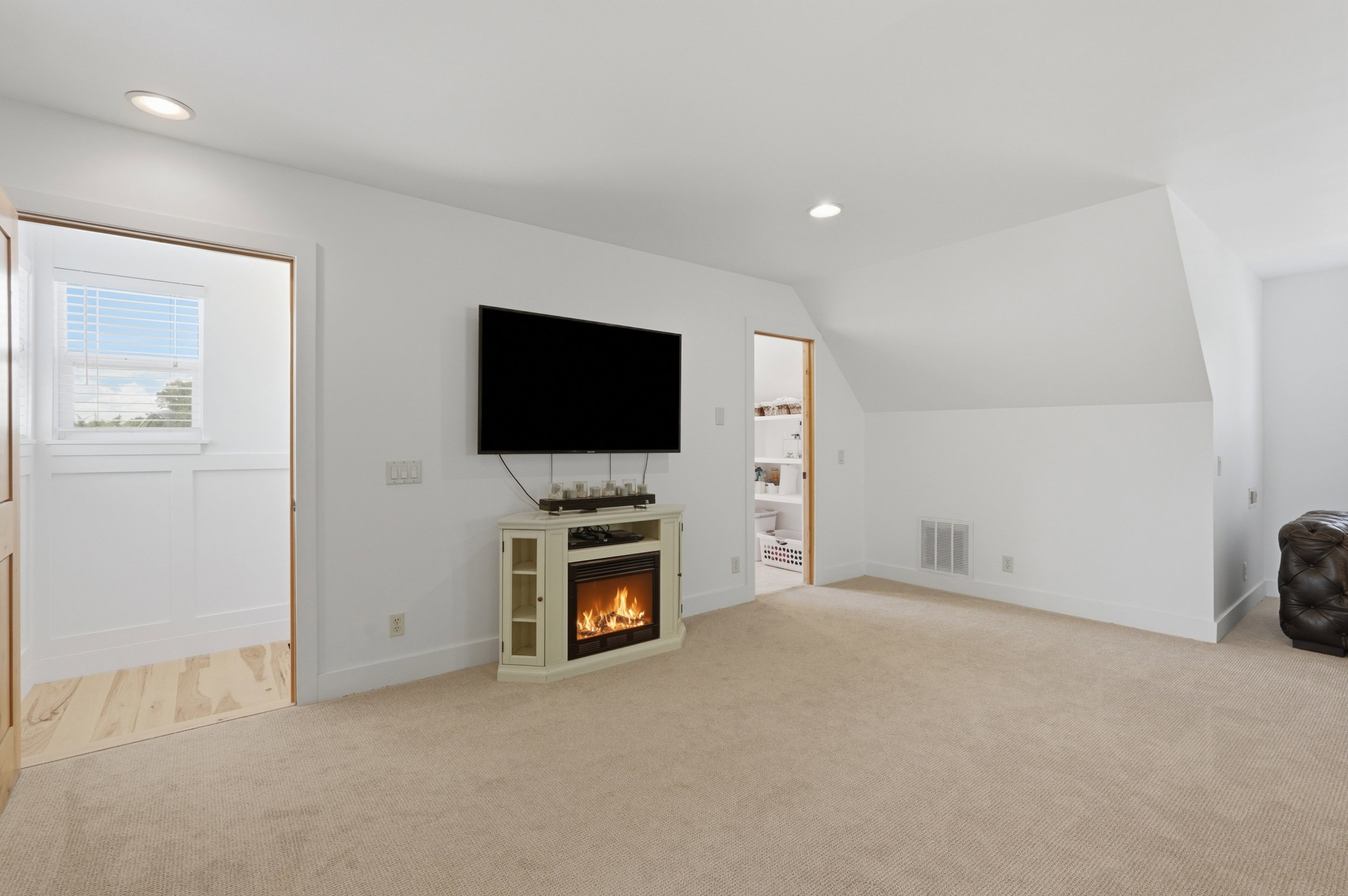 Carpeted room featuring a corner electric fireplace, recessed lighting, and white walls with an angled ceiling