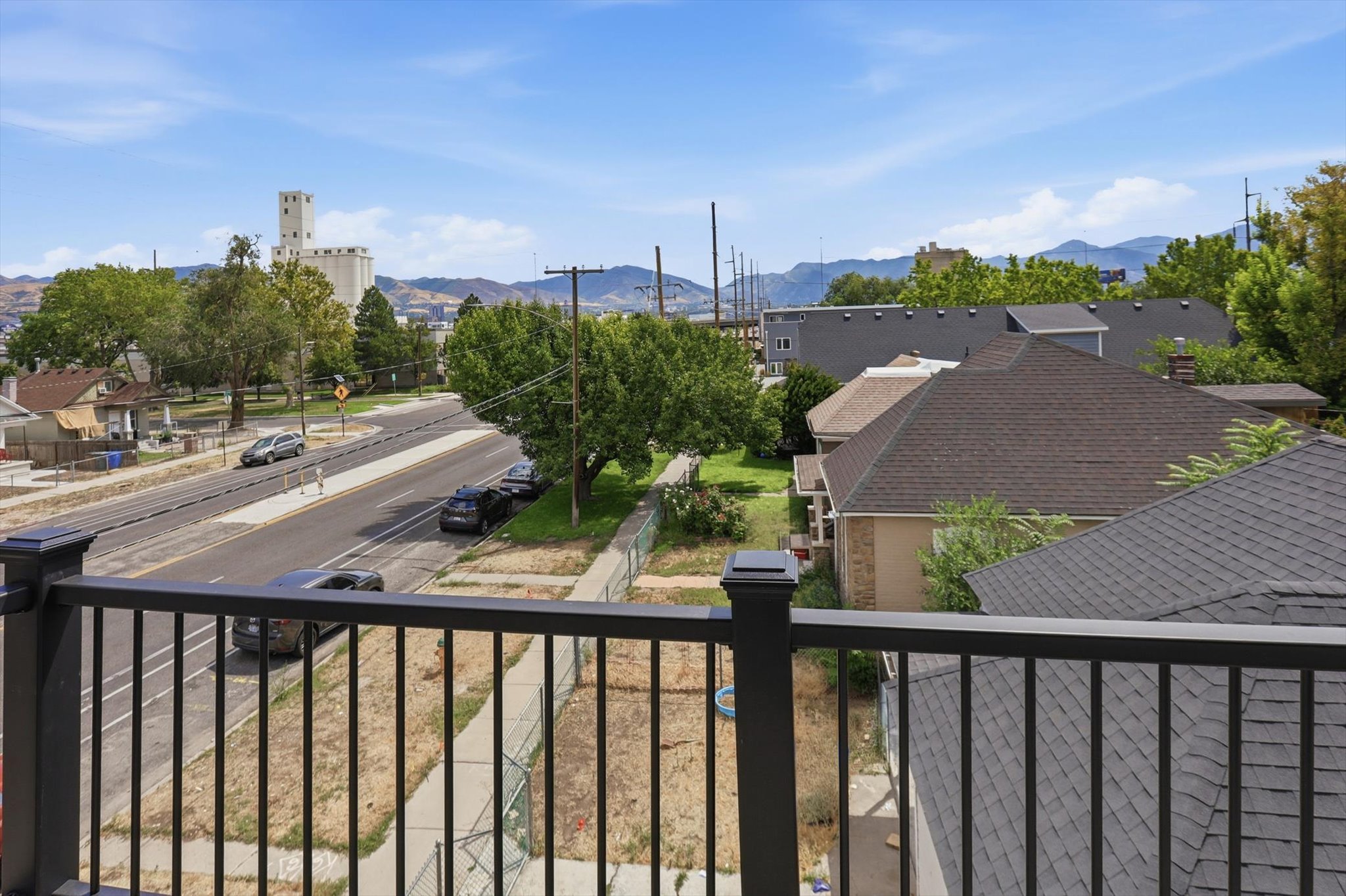 Balcony railing with a backdrop of a public thoroughfare, distant mountain range, and scattered structures