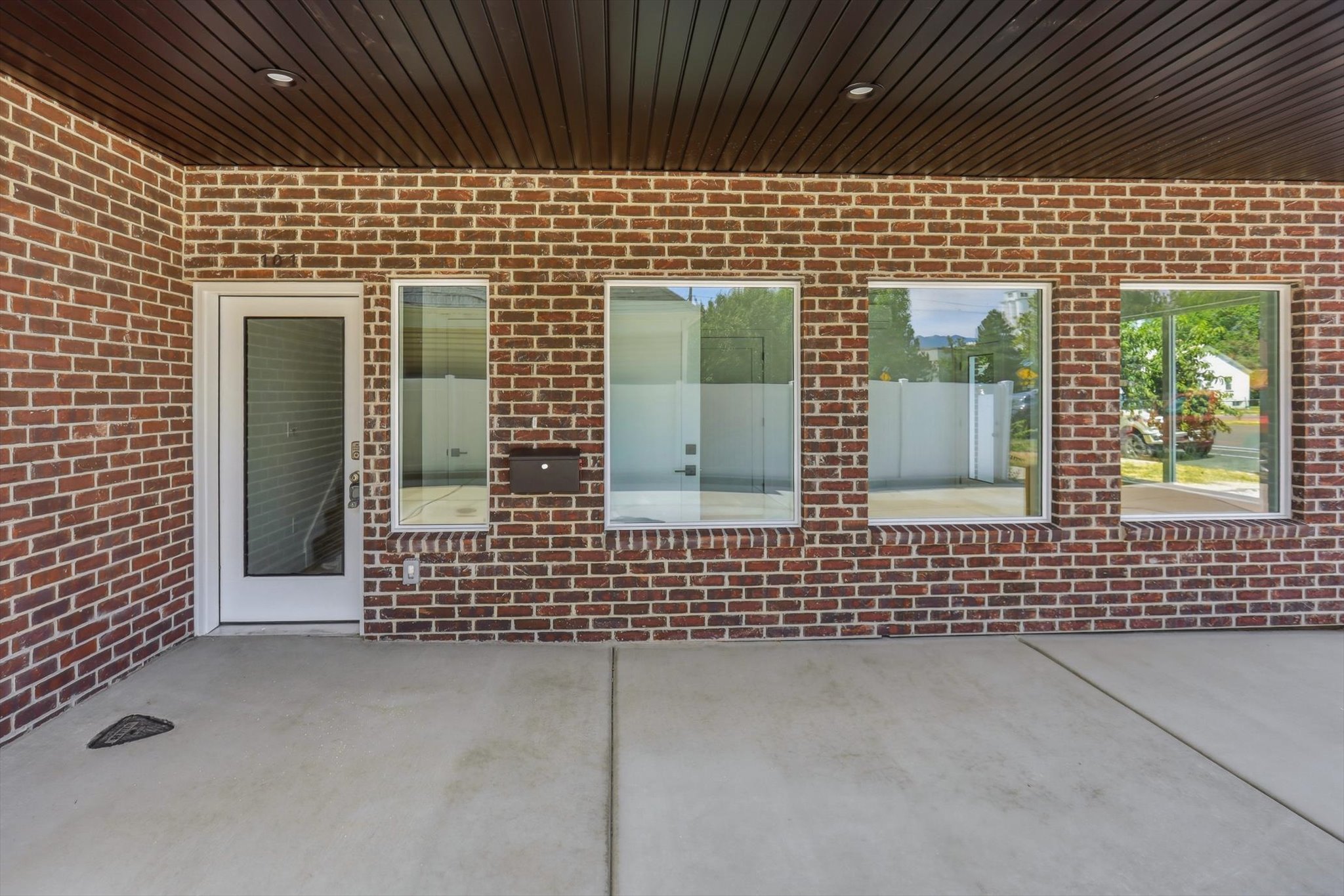 Brick exterior with a covered concrete patio, featuring a white entry door with a frosted glass panel, and multiple clear glass windows