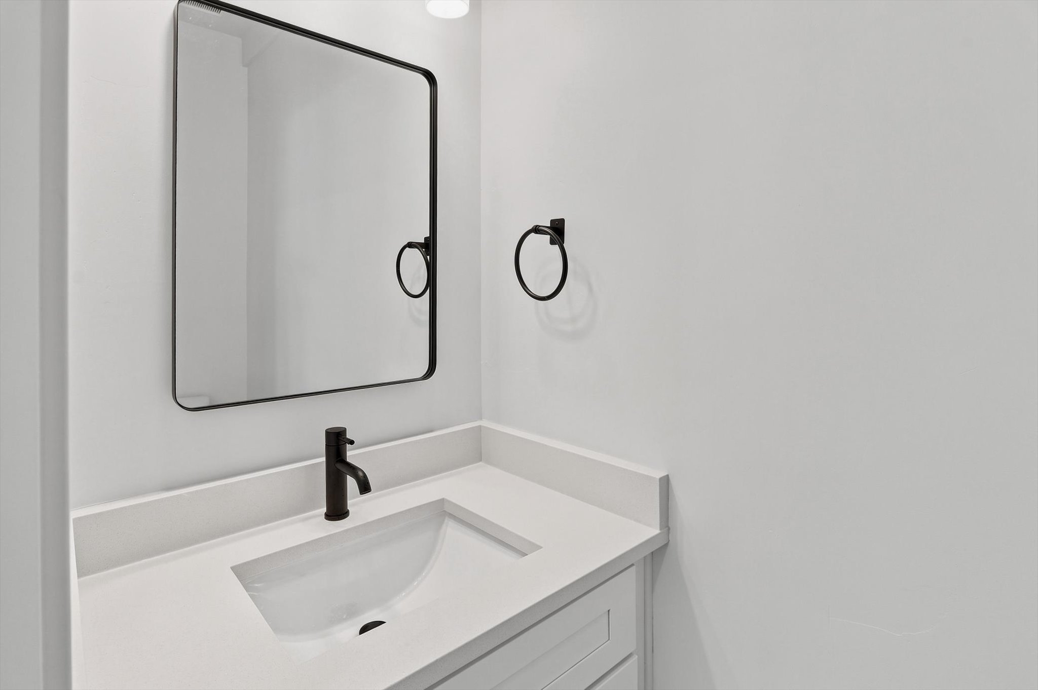 Modern vanity featuring an integrated sink with a matte black faucet, a framed rectangular mirror, and a coordinating matte black towel ring