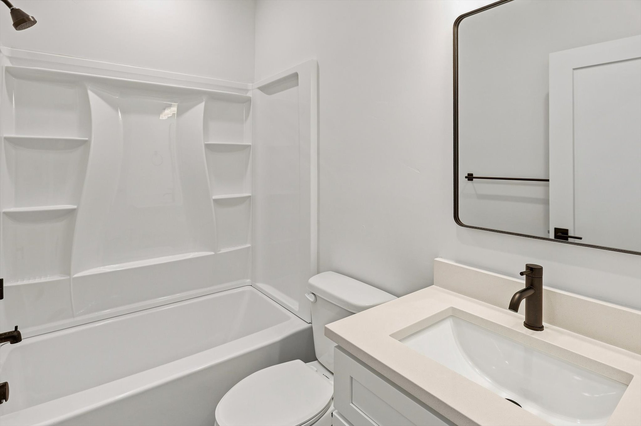 Bathroom featuring a white bathtub with integrated shelving, a white vanity with a light-colored countertop, and a rectangular undermount sink