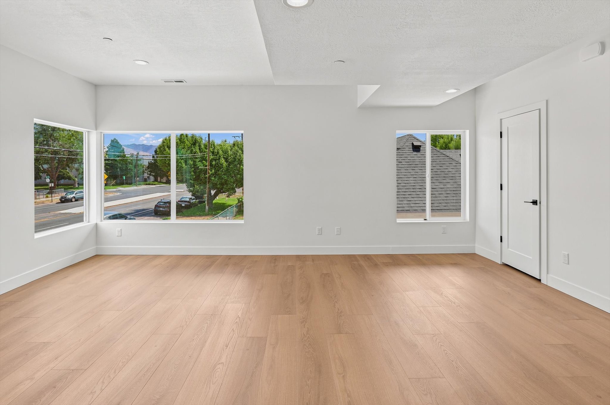 Spacious room featuring light wood-finish flooring, recessed lighting, multiple windows, and a crisp white color palette