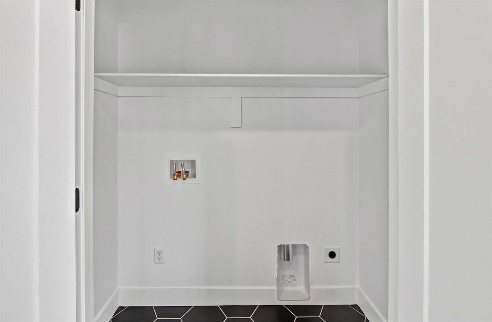 Laundry closet featuring a black hexagonal tile floor, white walls, and a built-in shelf