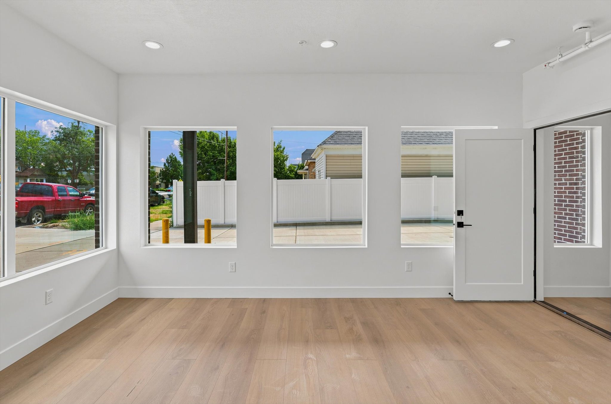 Spacious room featuring multiple windows, recessed lighting, wood-finish flooring, white baseboards, and a white interior door with black hardware