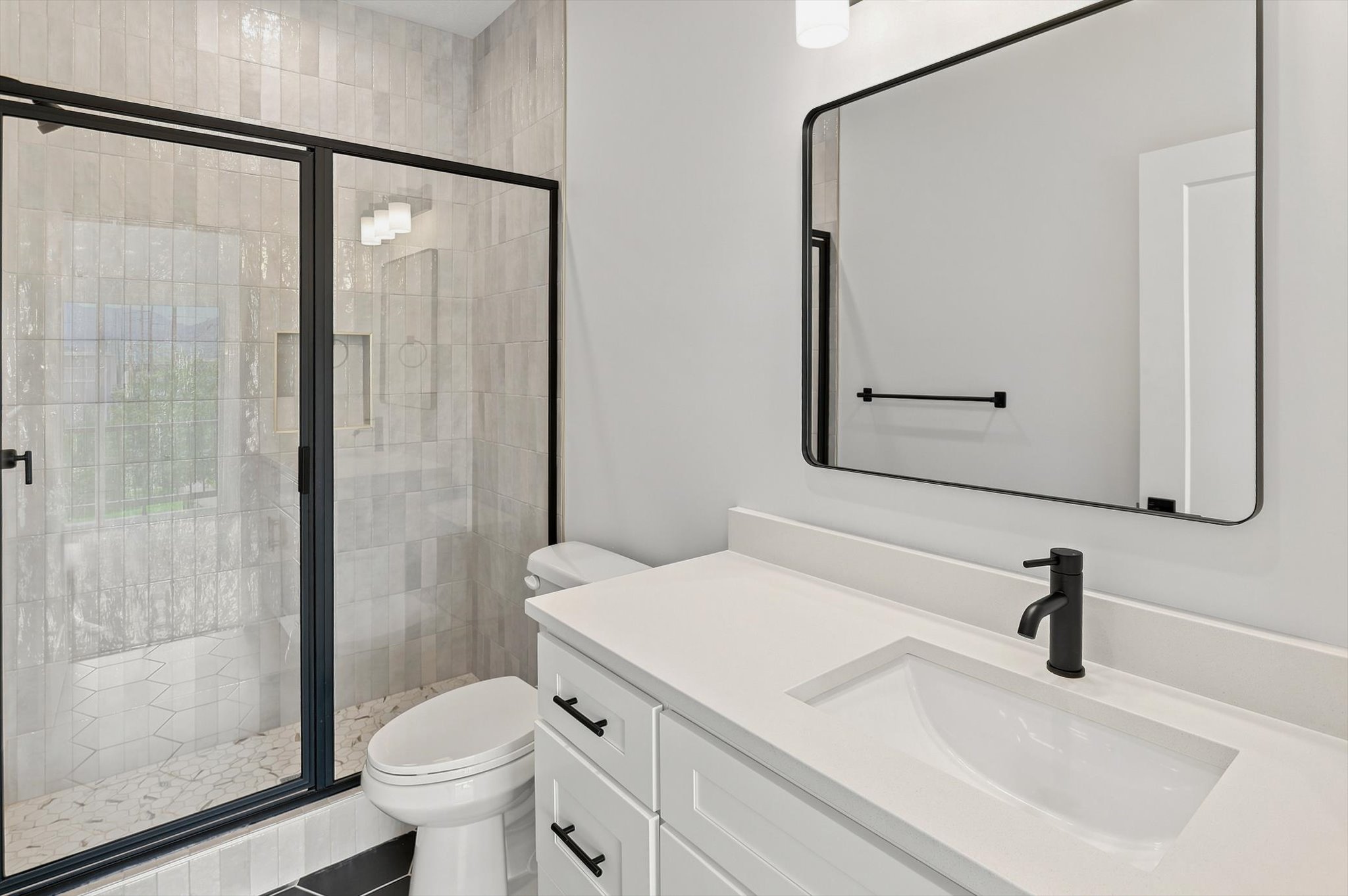 Contemporary bathroom featuring a frameless glass shower enclosure with matte black trim, a white vanity with integrated sink, a rectangular mirror, and matte black fixtures