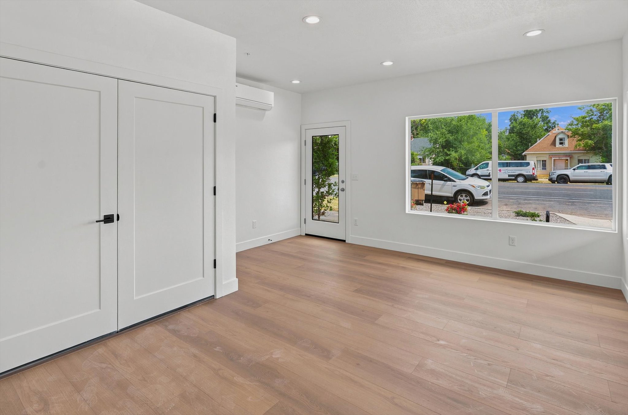 Bright open-concept space featuring expansive street-facing windows, wood-finish flooring, and recessed lighting