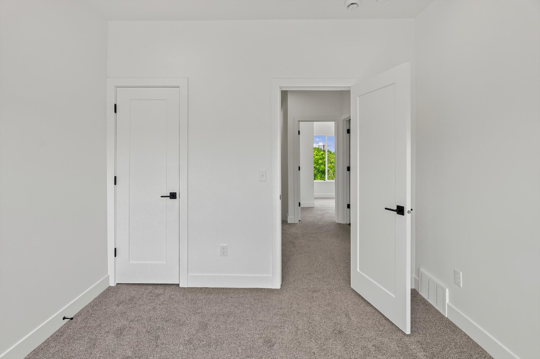 Interior space featuring neutral wall paint, gray carpeting, a flat panel door with black hardware, and white baseboards