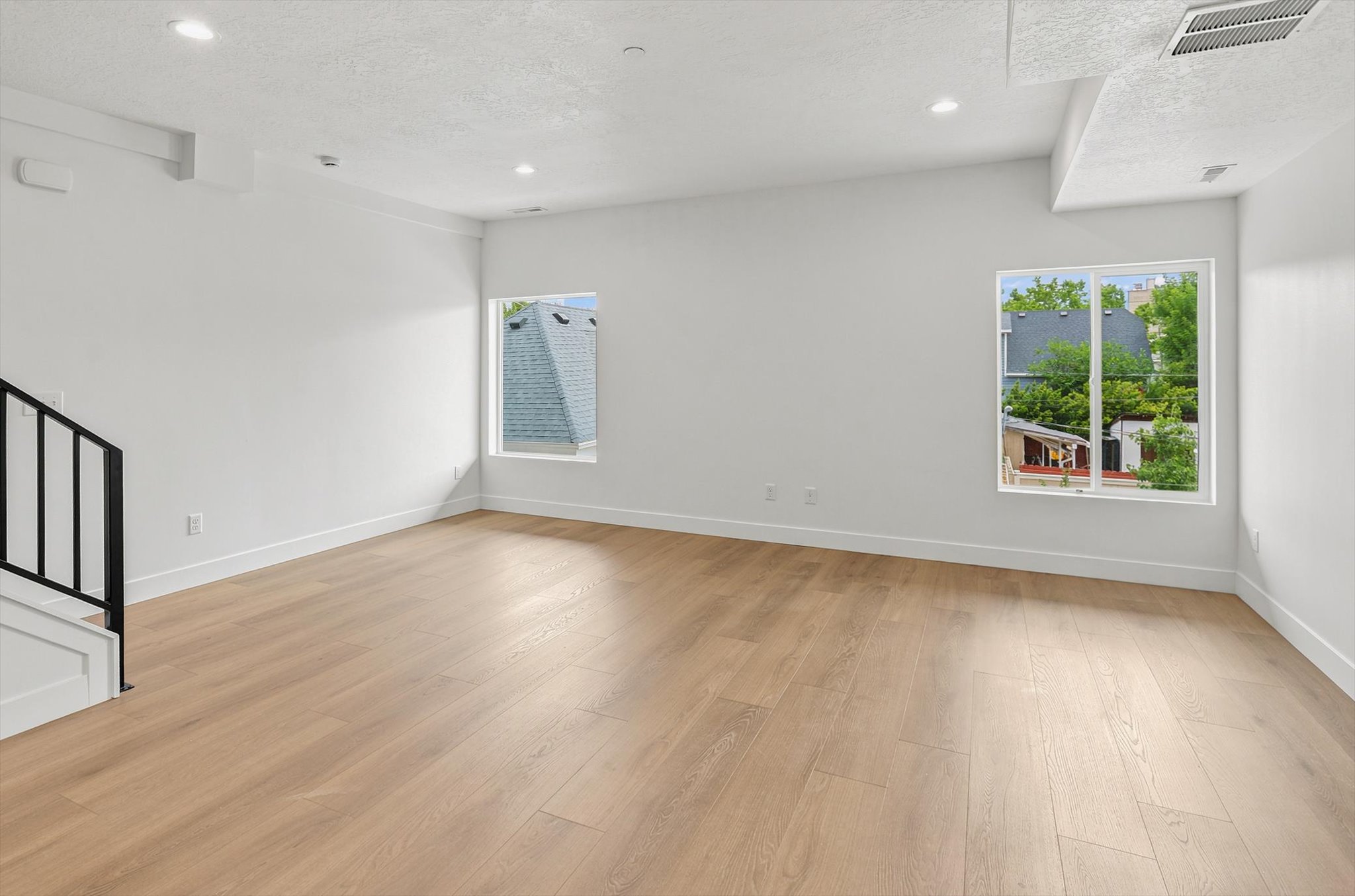 Expansive interior space featuring wood-finish flooring, two windows with white trim, and recessed ceiling lighting