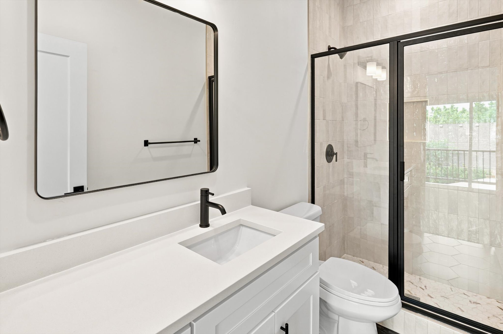 Bathroom featuring a white vanity with an integrated sink, matte black fixtures, a framed mirror, and a glass-enclosed shower with tiled walls and hexagonal floor tiles