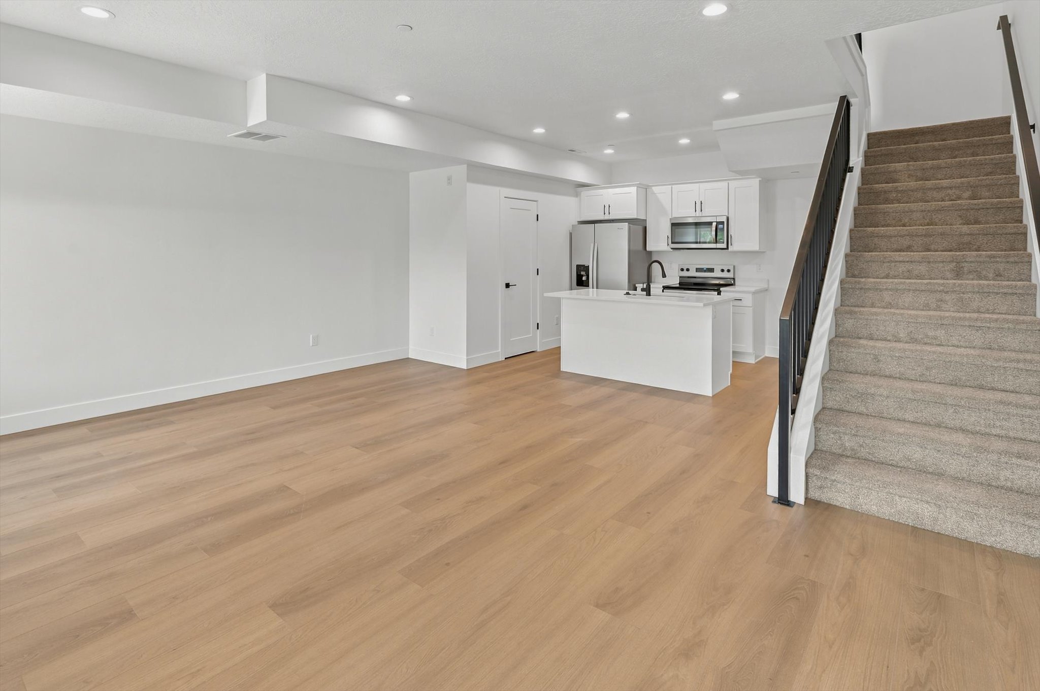 Open-concept living area featuring wood-finish flooring, recessed lighting, and a modern kitchen with white cabinetry and stainless steel appliances