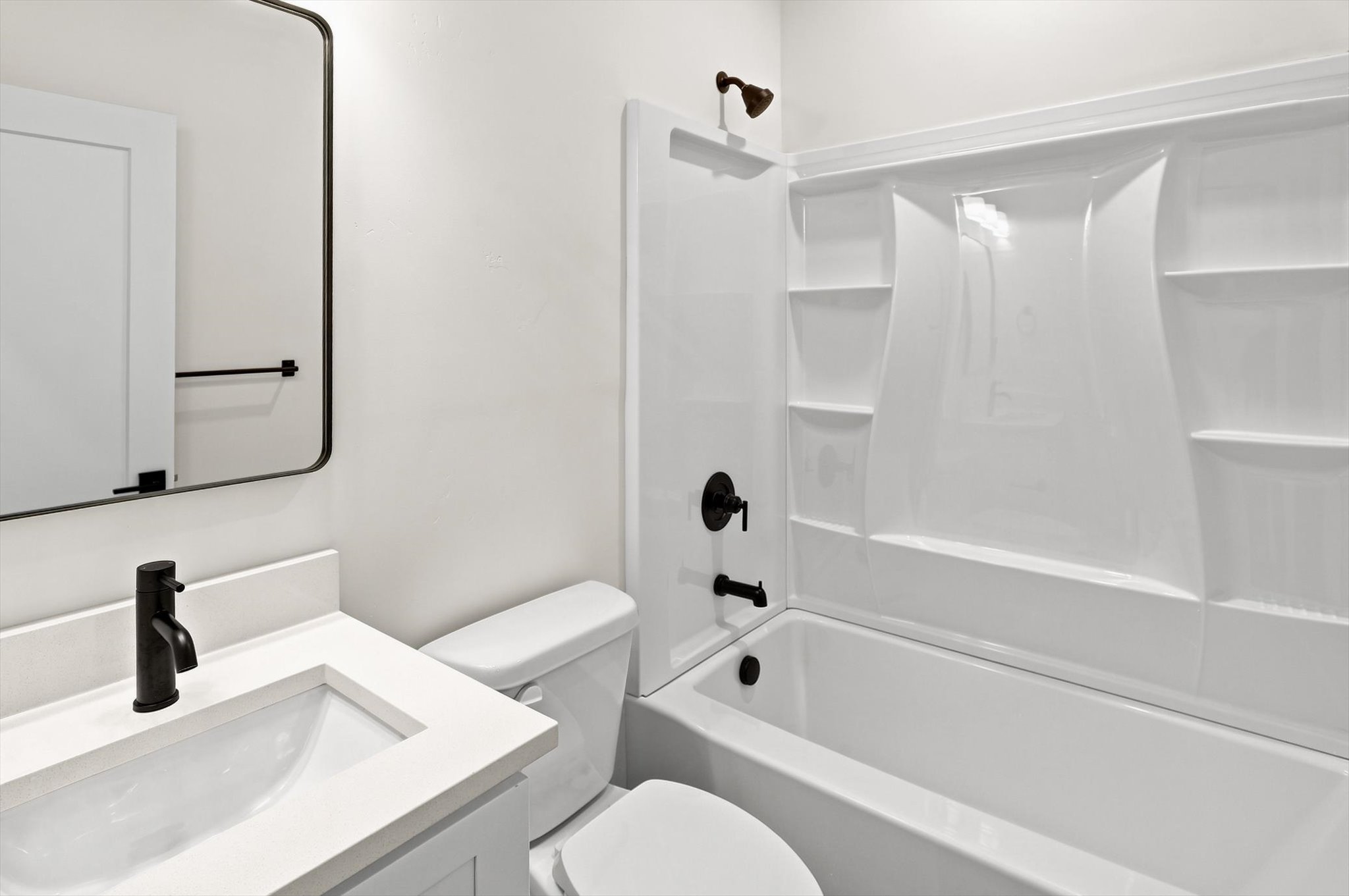Bathroom featuring a white vanity with an integrated sink, matte black faucet, and a rectangular framed mirror