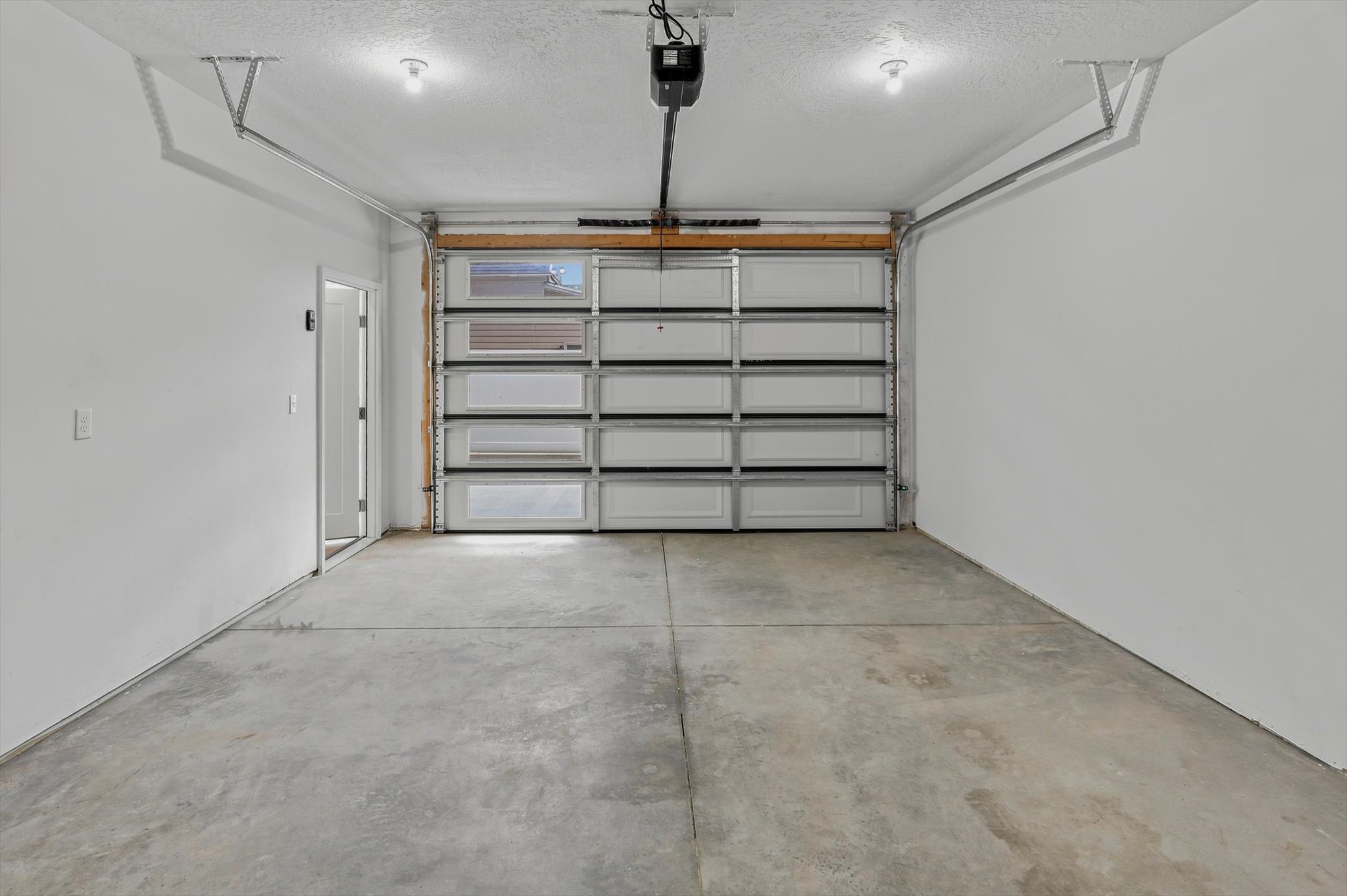 Spacious garage featuring a concrete floor, bright white walls, and a multi-panel garage door with frosted window inserts