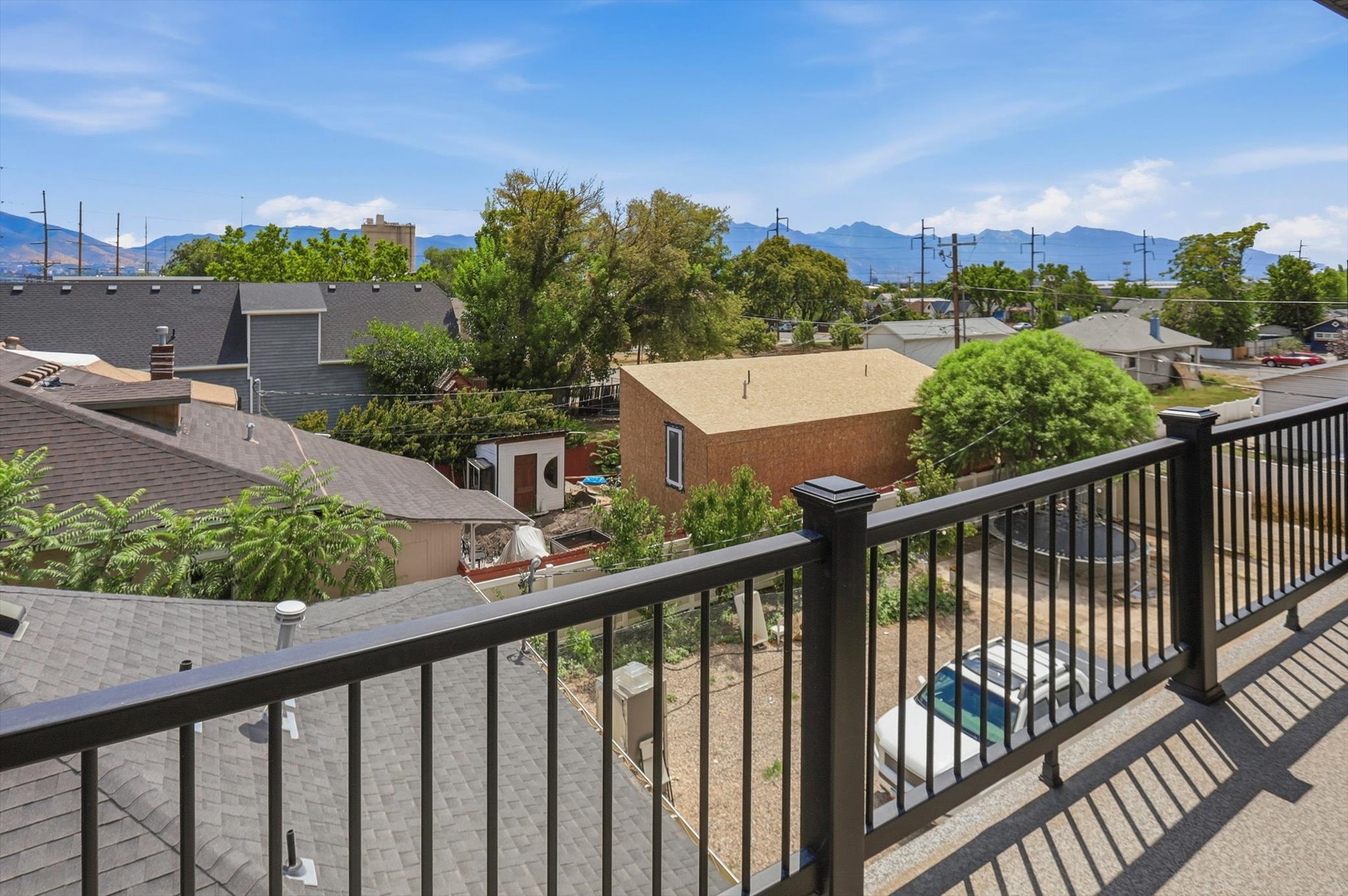 Upper-story balcony with black metal railing, offering expansive views of surrounding rooftops, mature trees, and distant mountains