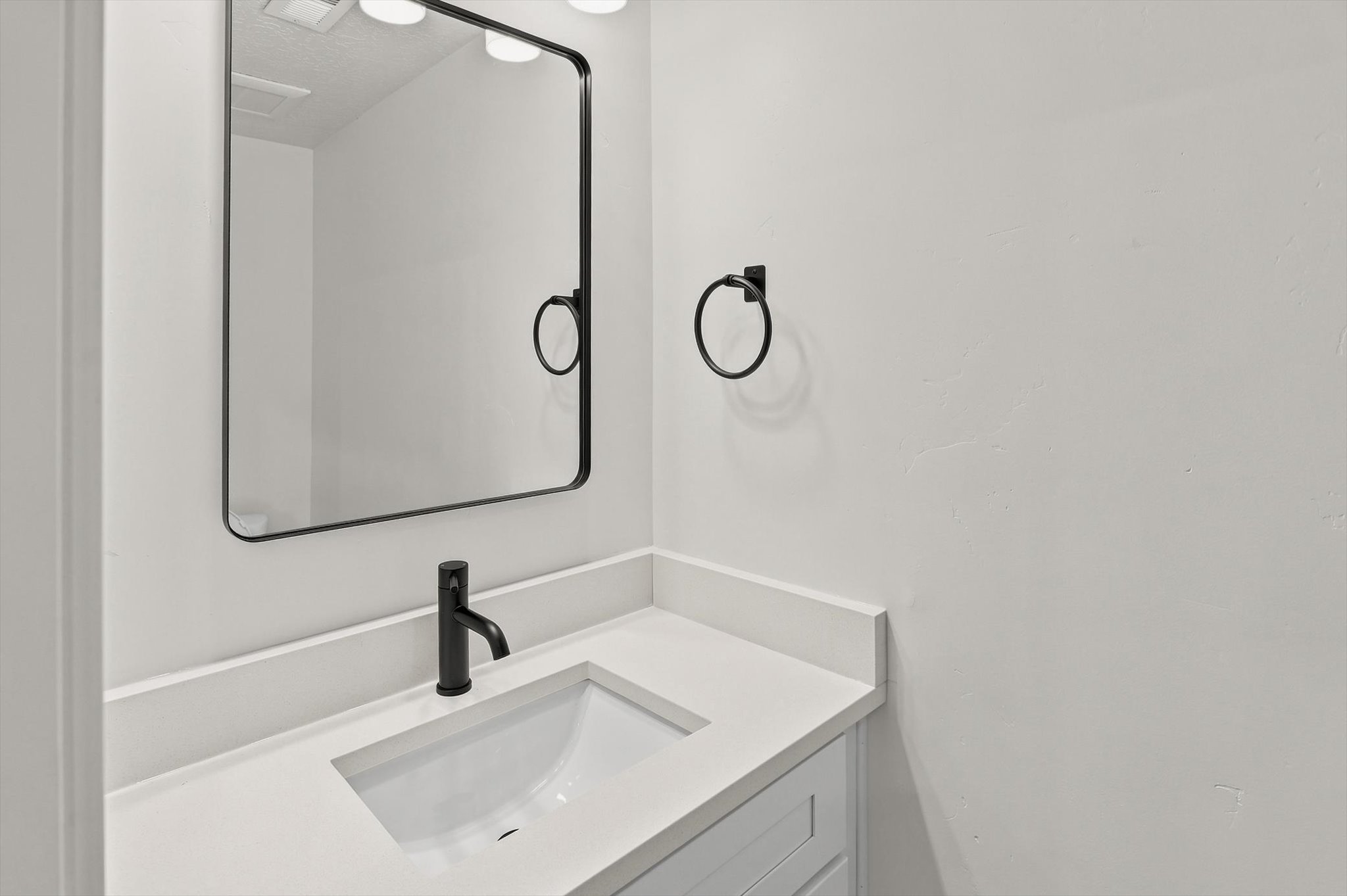 Bathroom vanity featuring a white countertop with an integrated sink, matte black faucet, and a rectangular mirror with a black frame