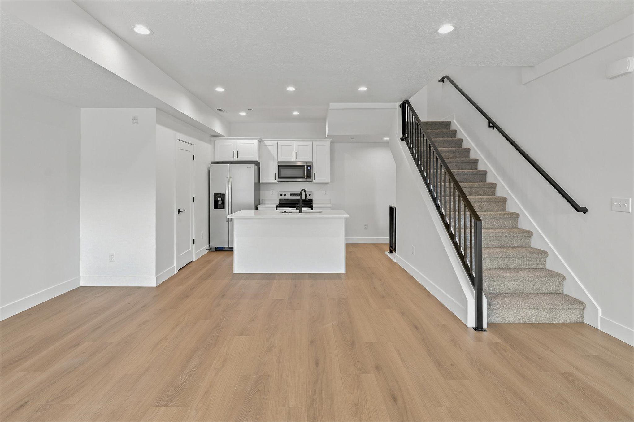 Open-concept living space featuring light wood-finish flooring, recessed lighting, and a modern kitchen with white cabinetry