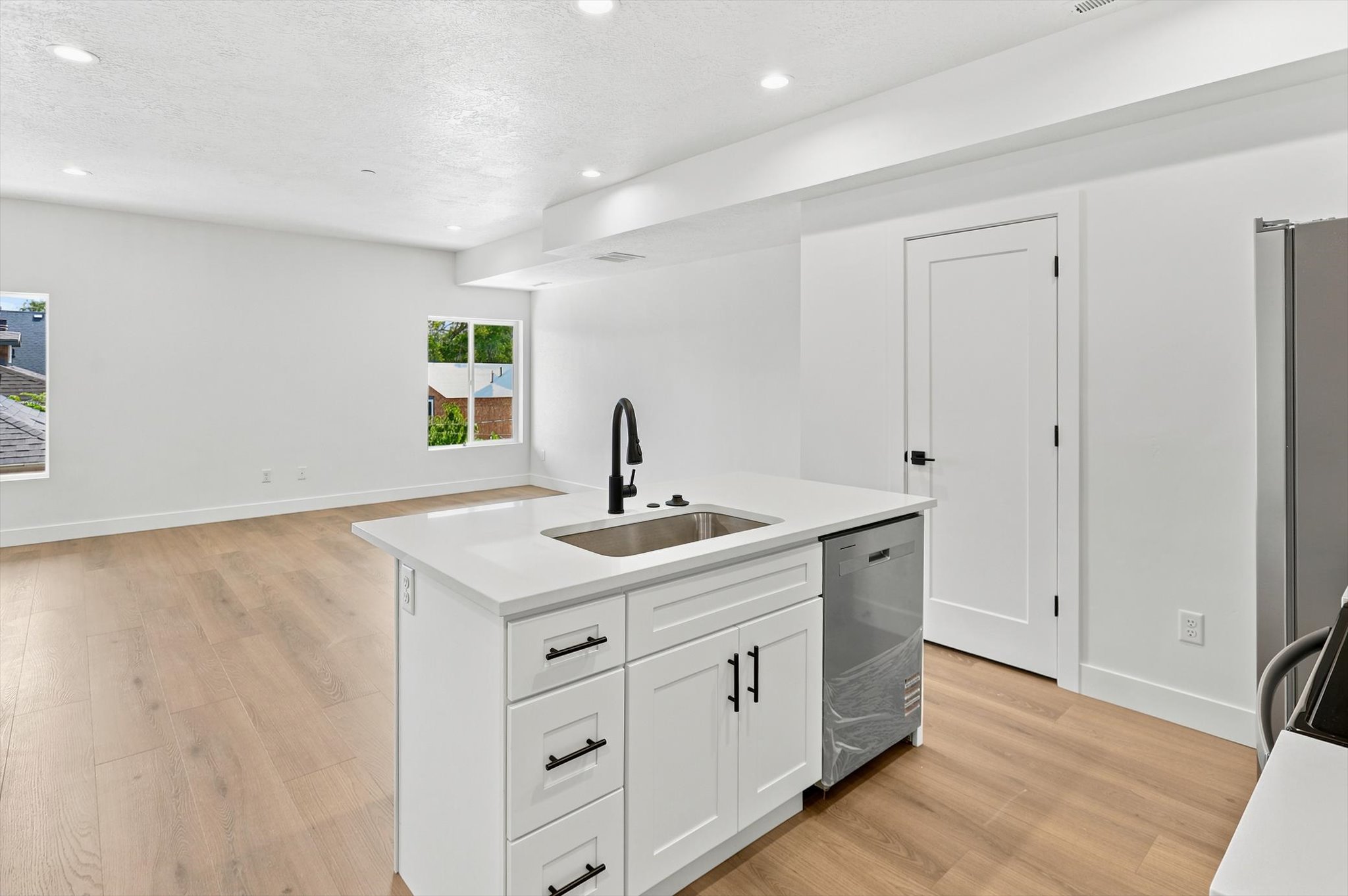 Open-concept living space featuring a central island with a stainless steel sink, a matte black faucet, and white cabinetry with dark hardware