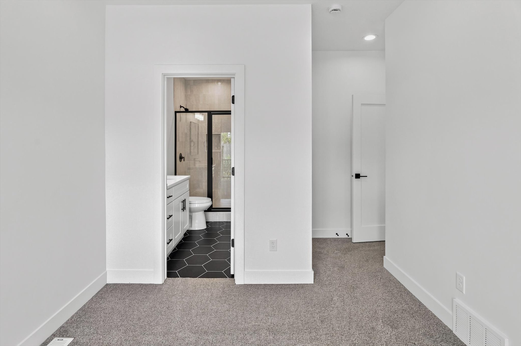 Bathroom featuring a white vanity with sink, dark hexagon floor tiles, glass-enclosed shower with black trim, and light-toned wall tiling