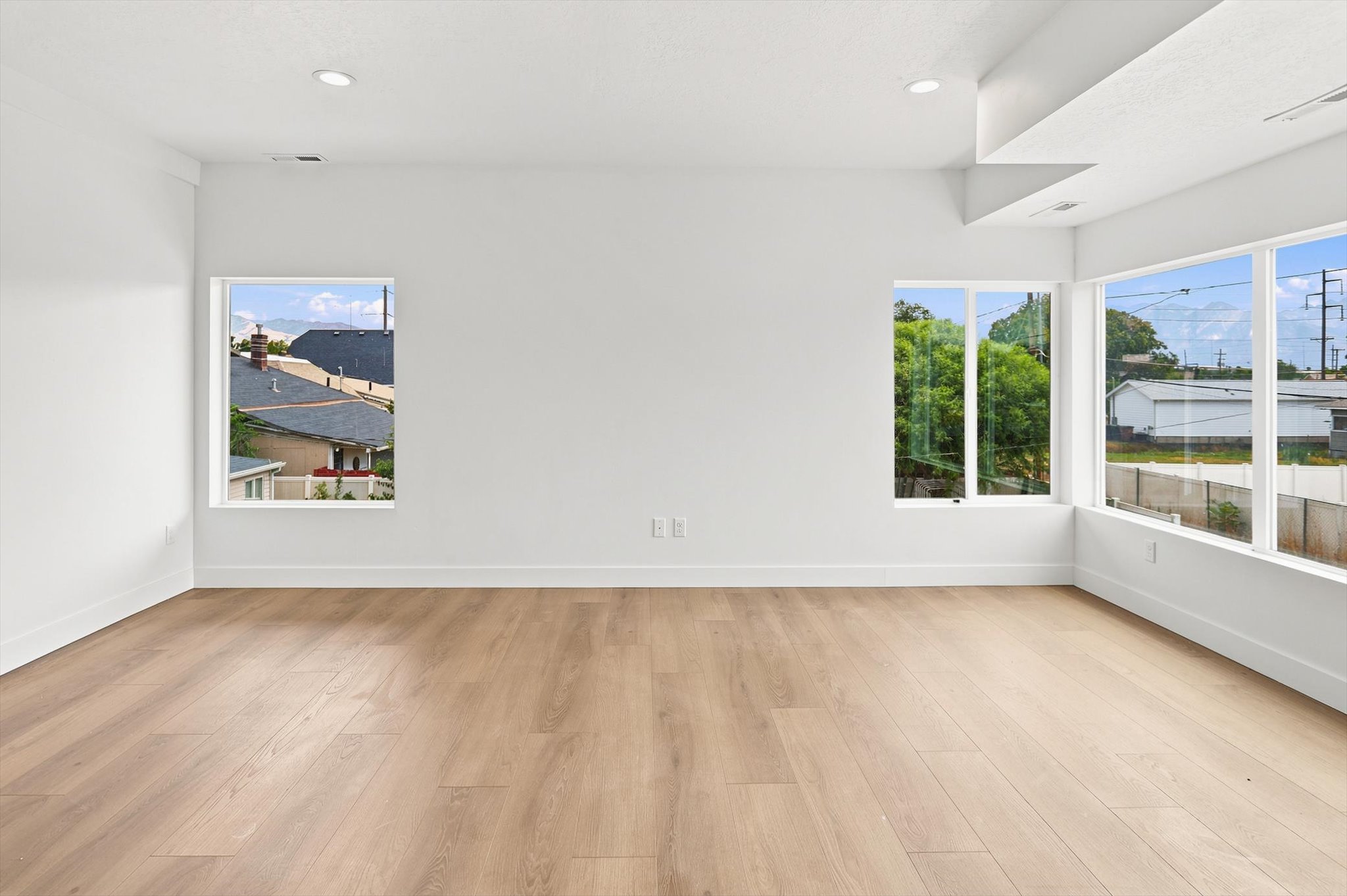 Spacious interior with light wood-finish flooring, white walls, multiple large windows, recessed ceiling lighting, and crisp white baseboards