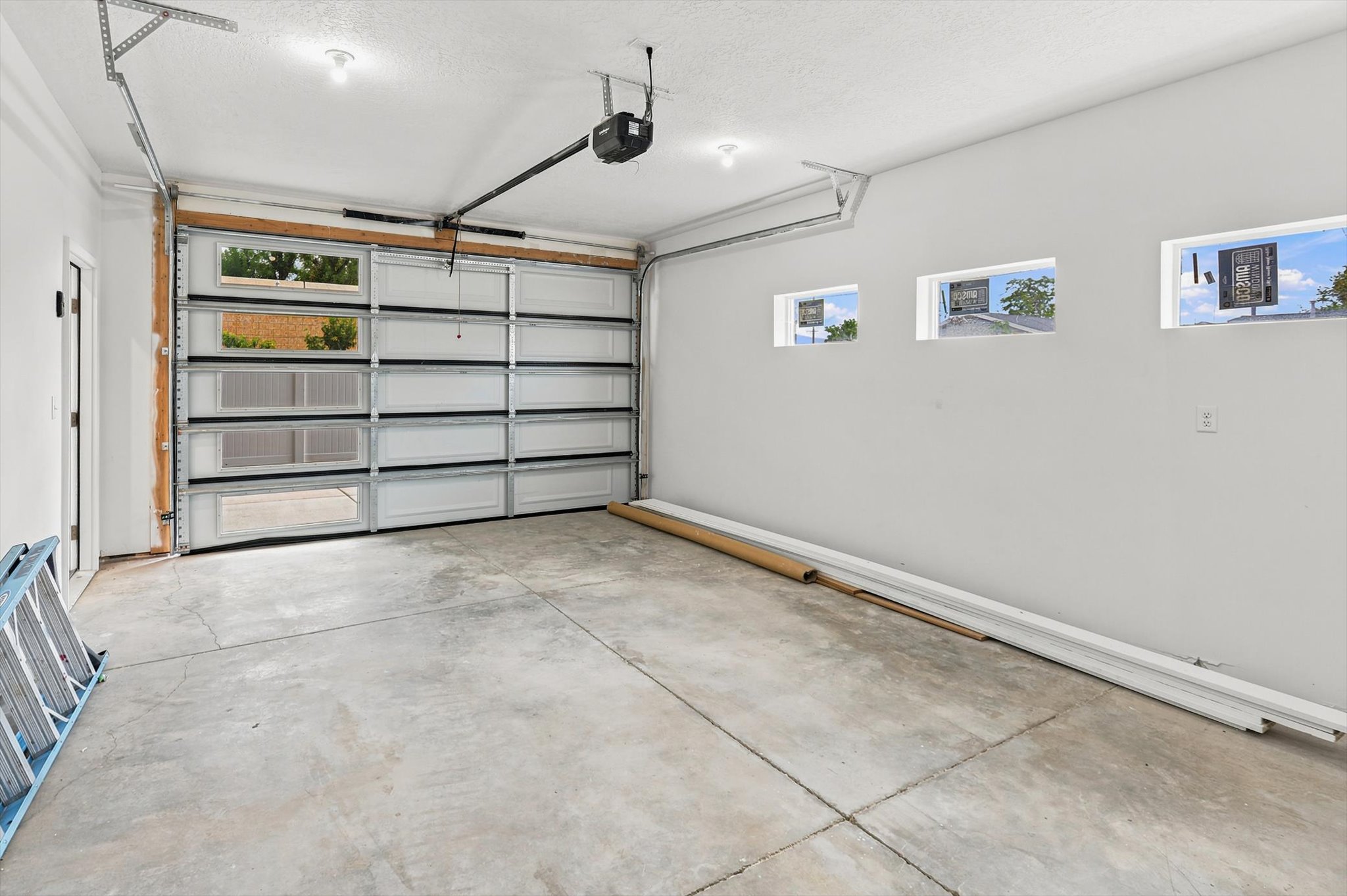 Spacious garage featuring a modern overhead door with clear glass panels, concrete flooring, three high-set windows, and recessed lighting