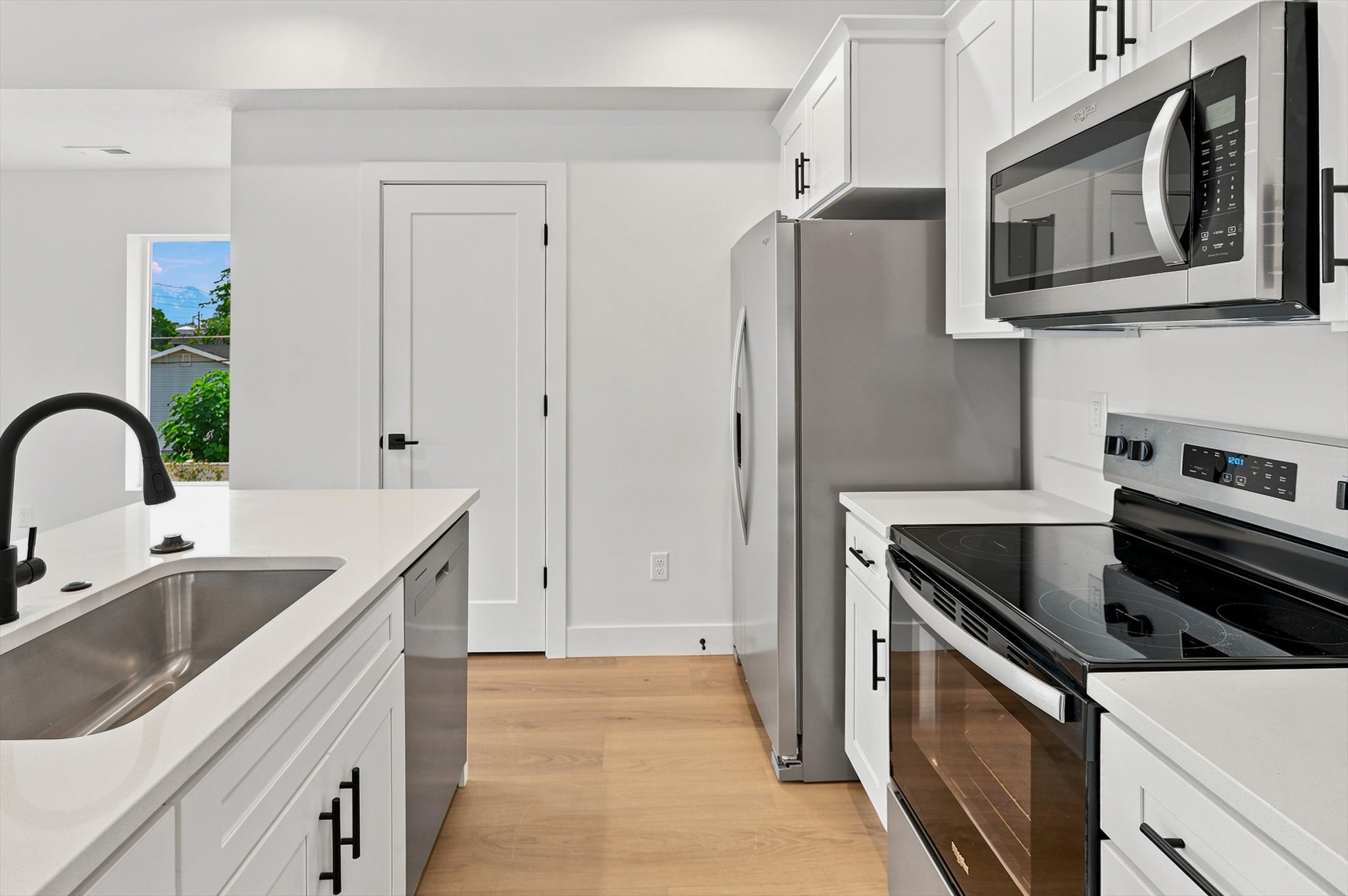 Modern kitchen featuring white shaker cabinetry, stainless steel appliances, light wood-finish flooring, and matte black fixtures