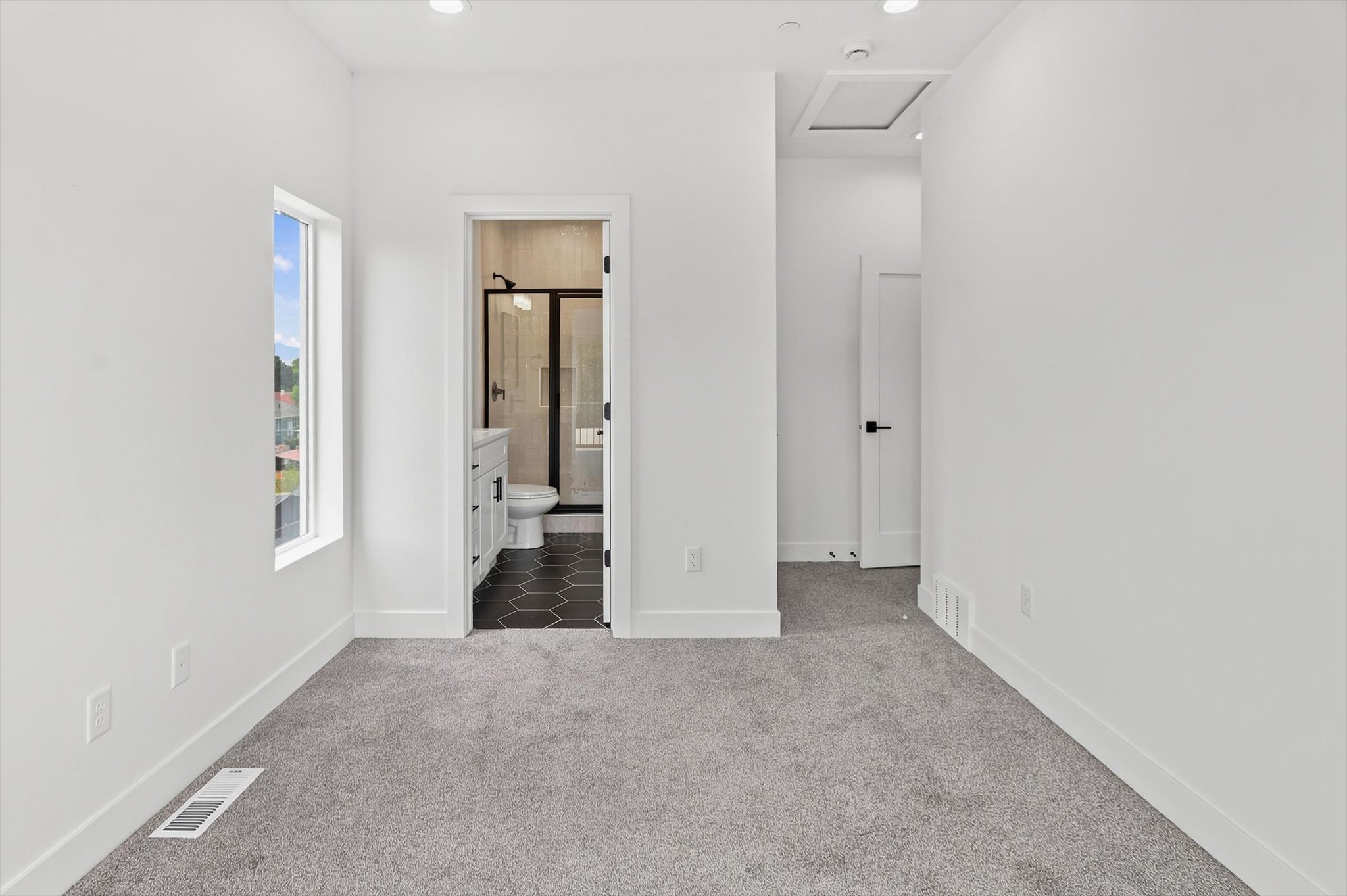 Carpeted room featuring a window with exterior views, recessed lighting, and a bathroom entry with black hexagonal floor tiles